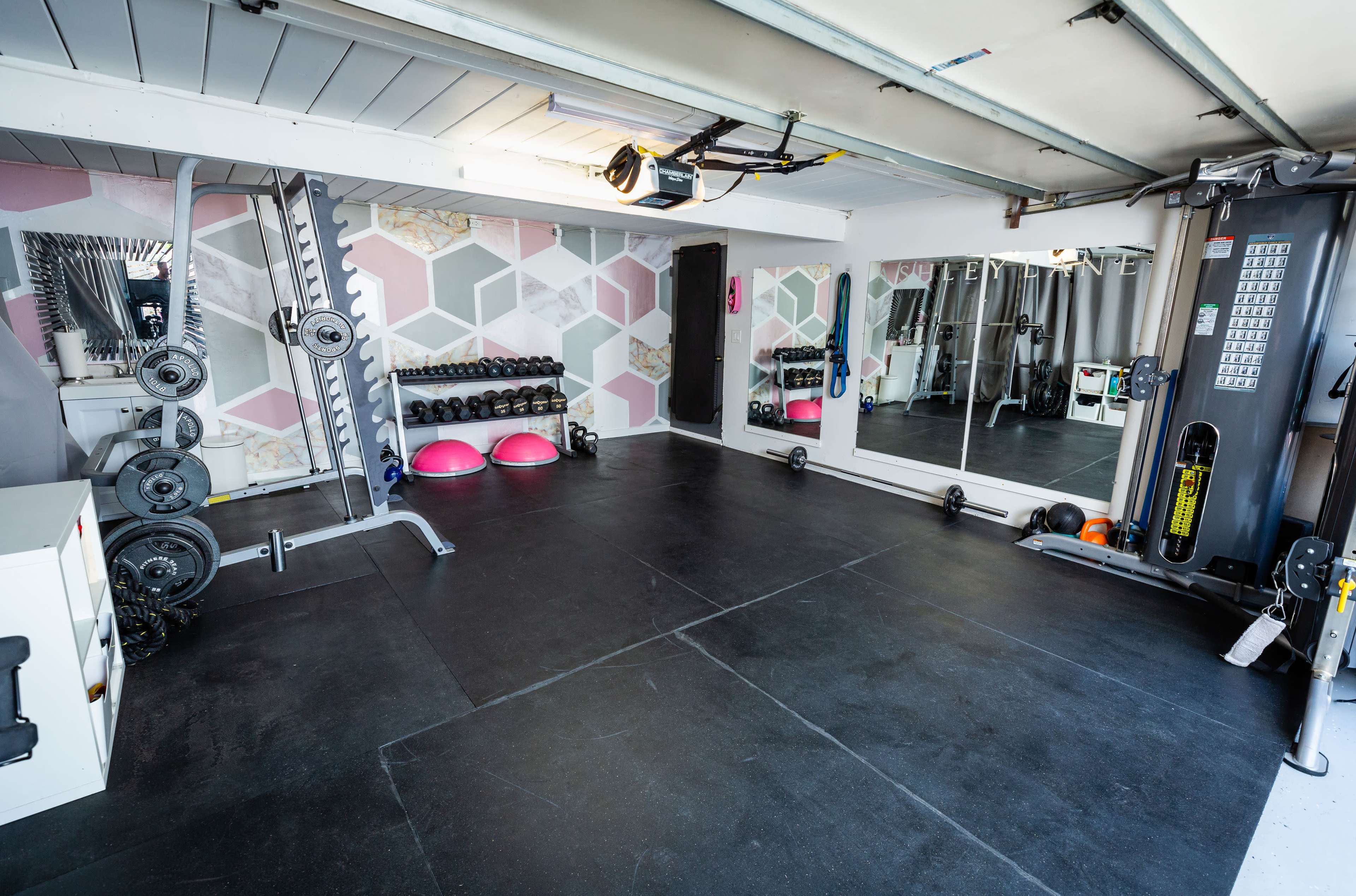 A gym interior with various weightlifting equipment, mirrors, and exercise balls arranged on a black rubber floor.