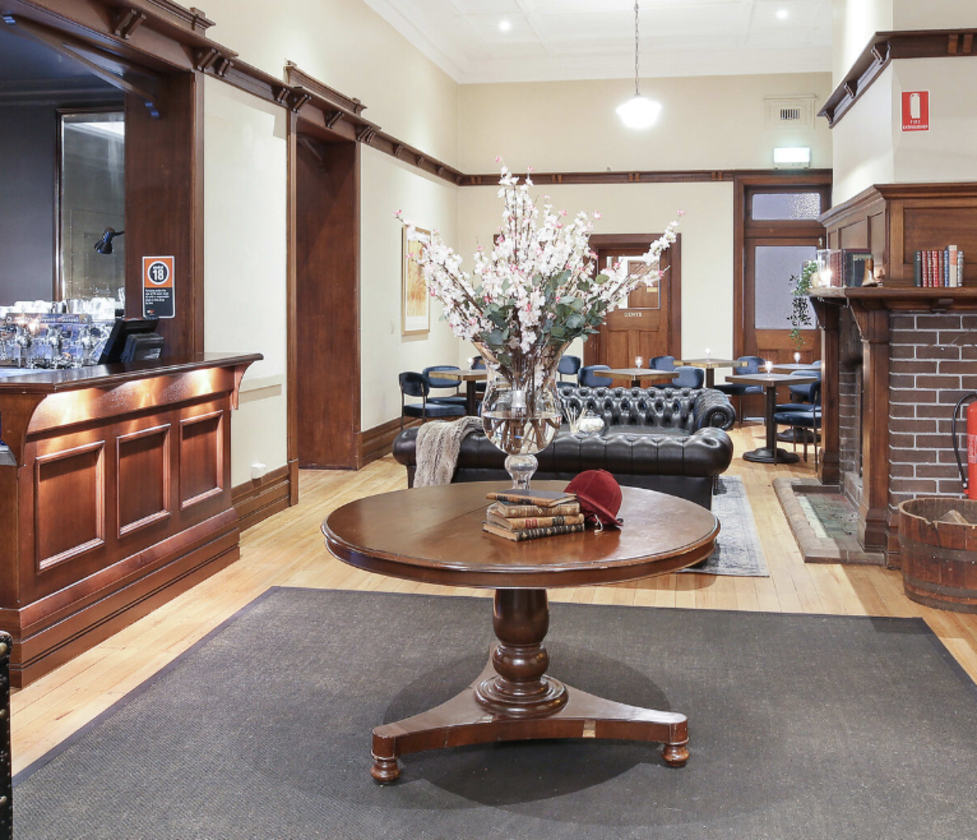 A lobby area featuring a round wooden table with a vase of flowers, surrounded by leather seating and a fireplace.