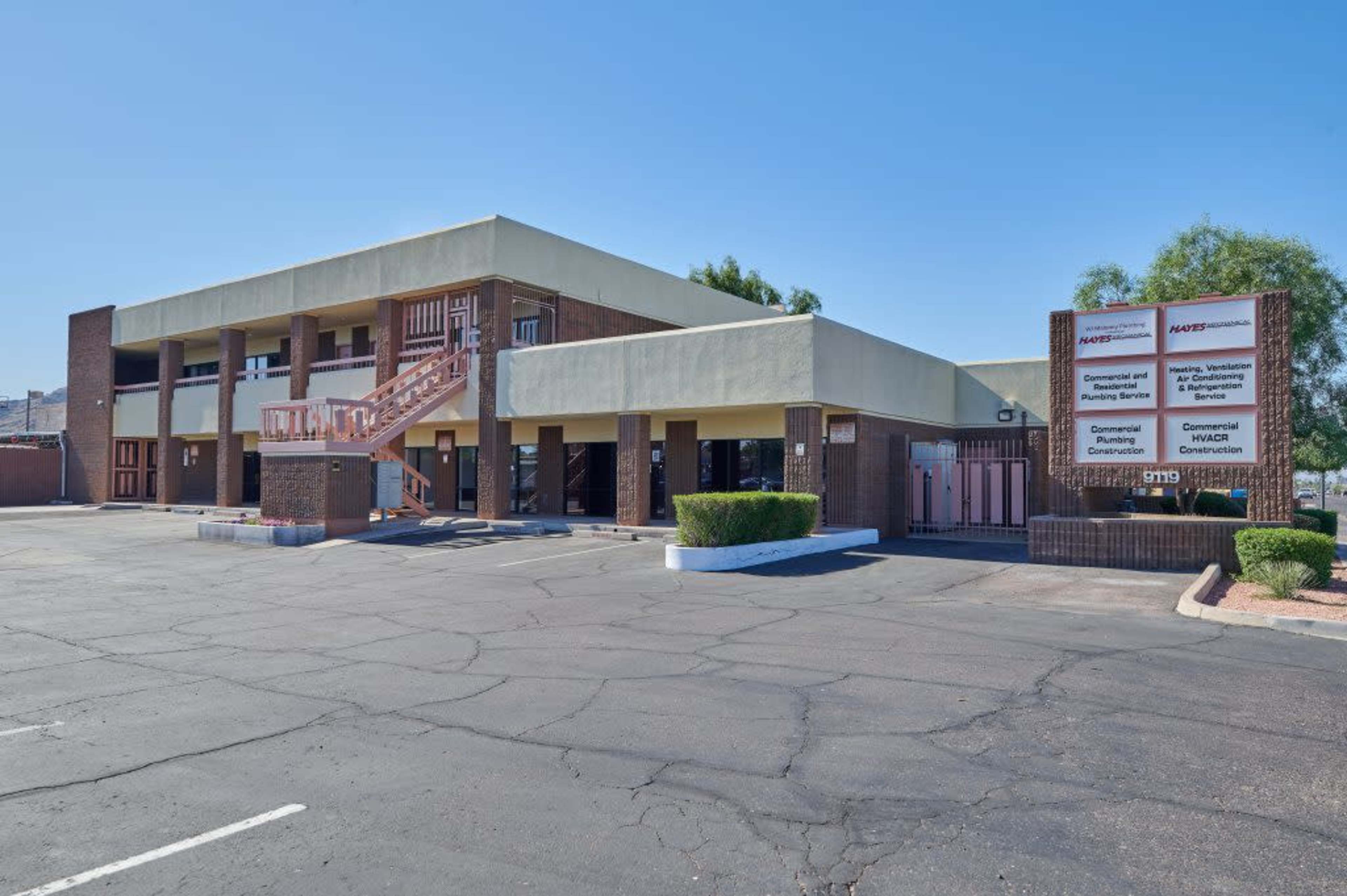 A two-story commercial building with a staircase on the side and a sign displaying various business services in front.