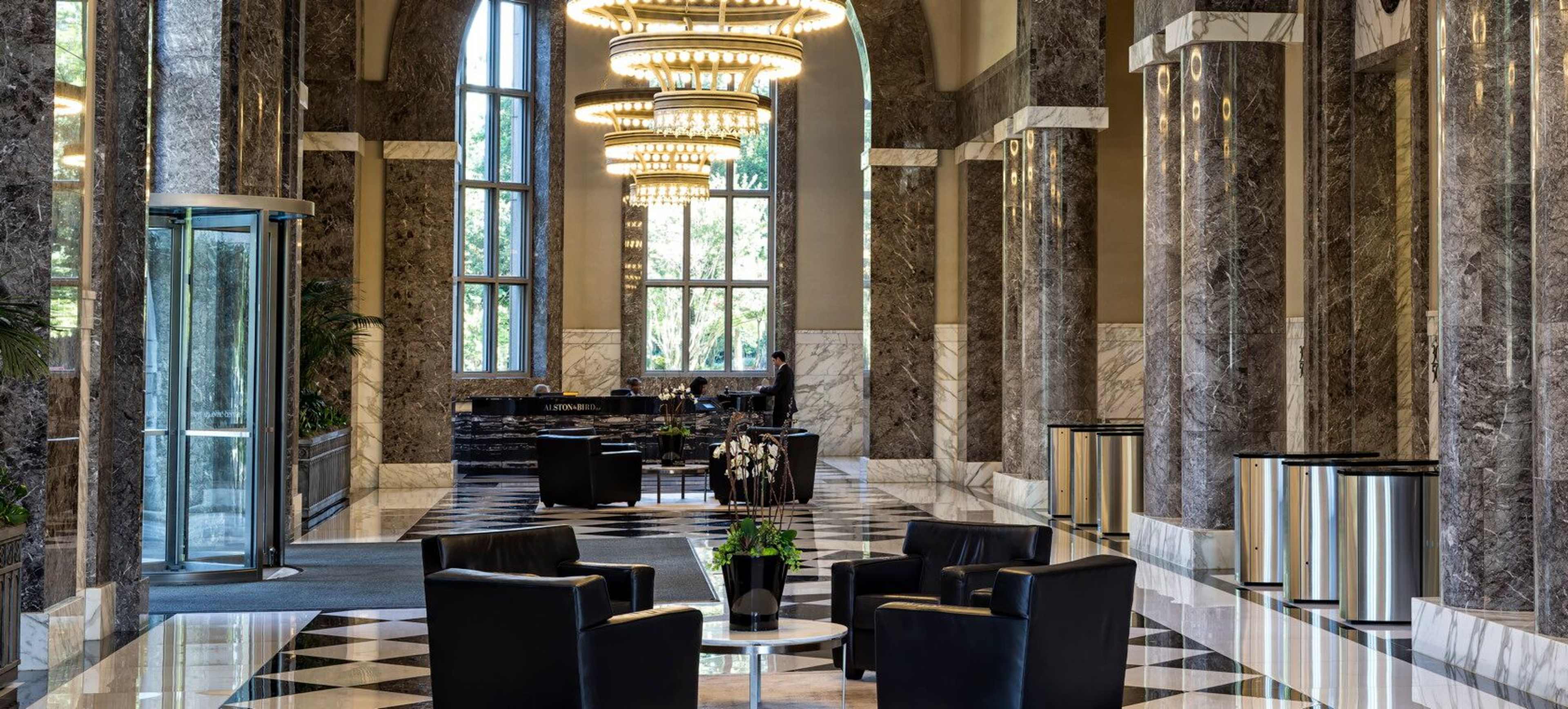 A luxurious lobby with marble columns, a checkered floor, and elegant chandeliers, featuring modern seating arrangements.