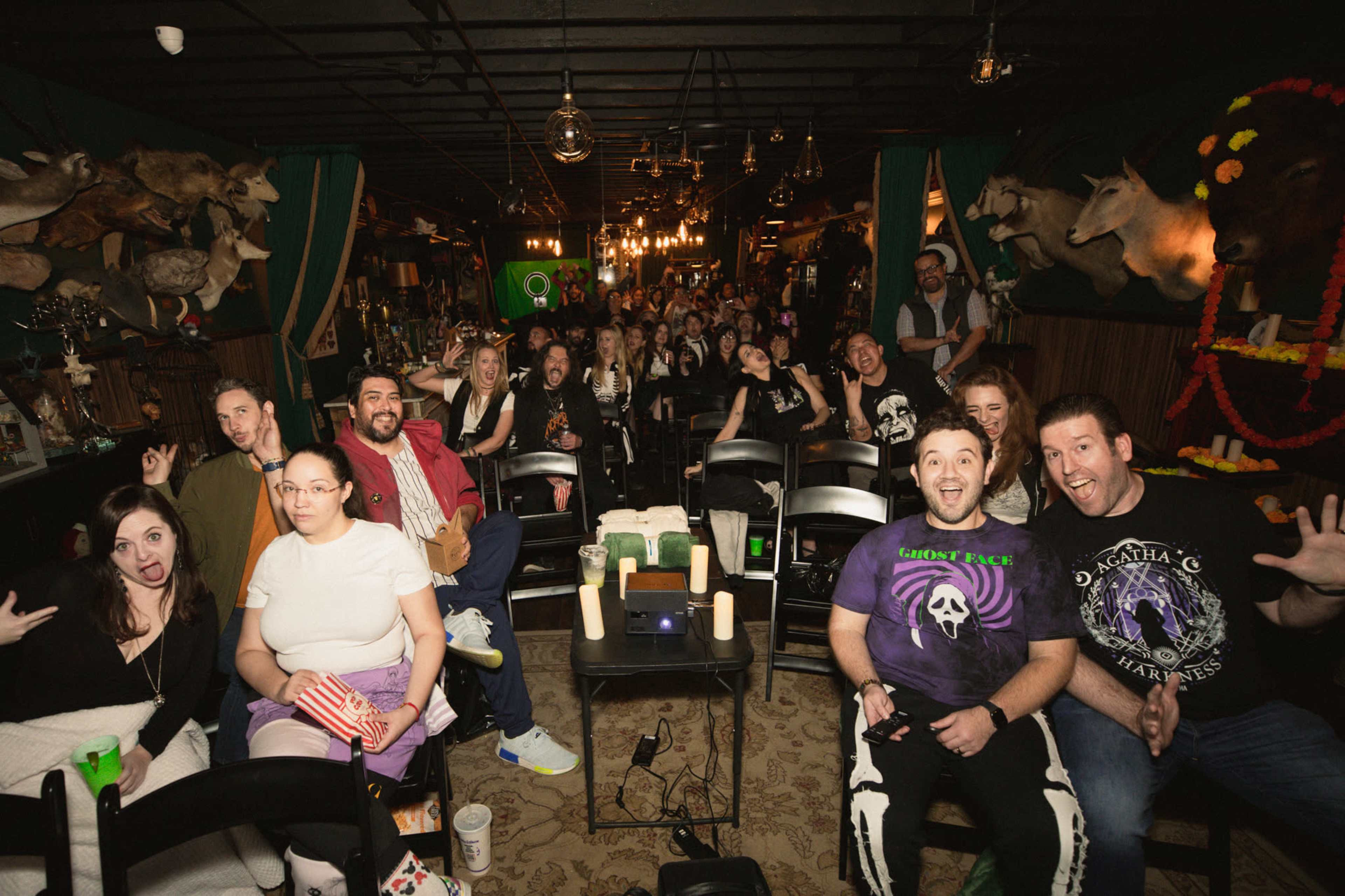 A crowded indoor venue with seating arranged for an event, featuring an audience of diverse individuals, some smiling and posing for the camera.