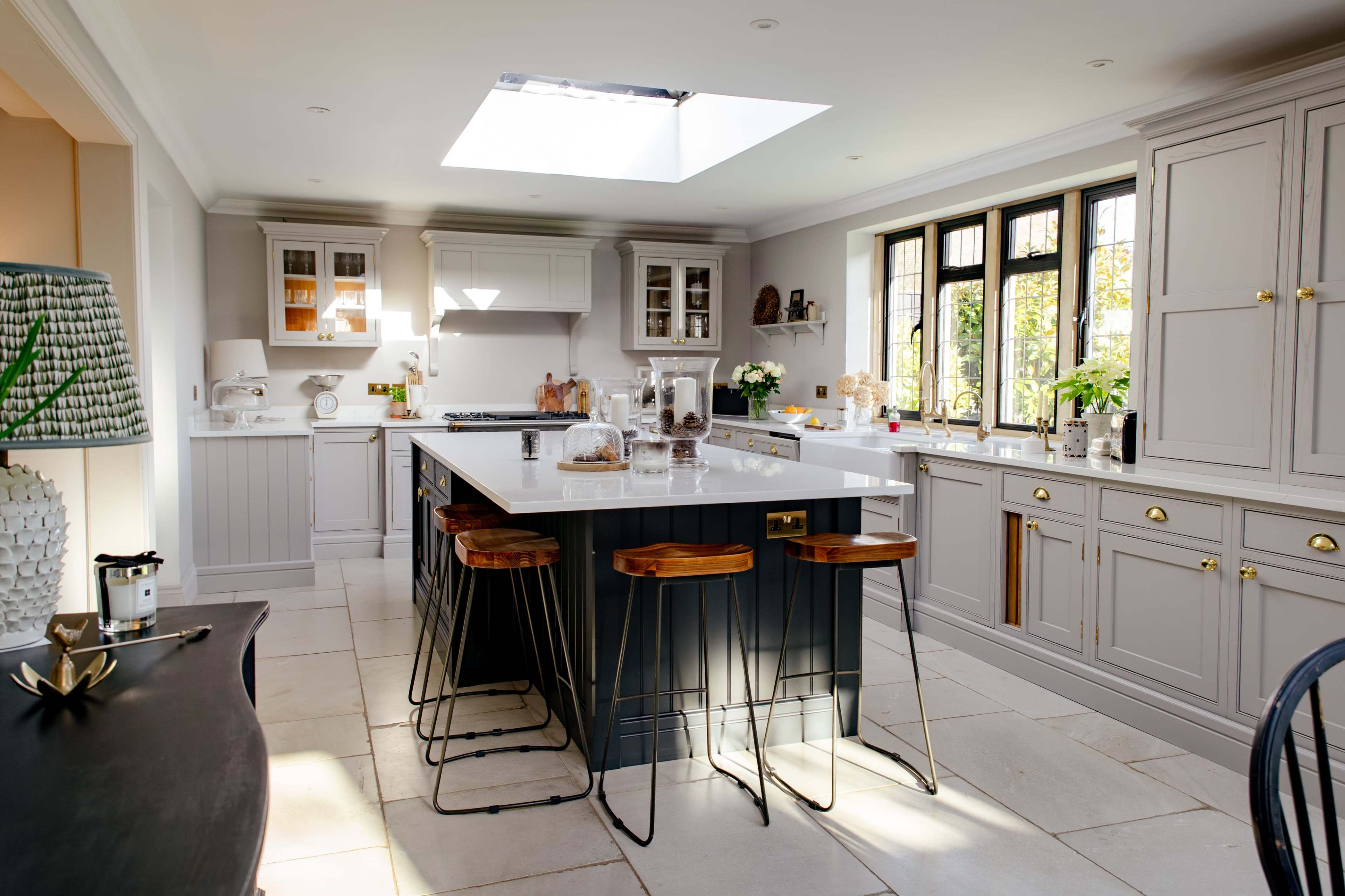 A modern kitchen features a central island with bar stools, large windows, and natural light coming in from a skylight.