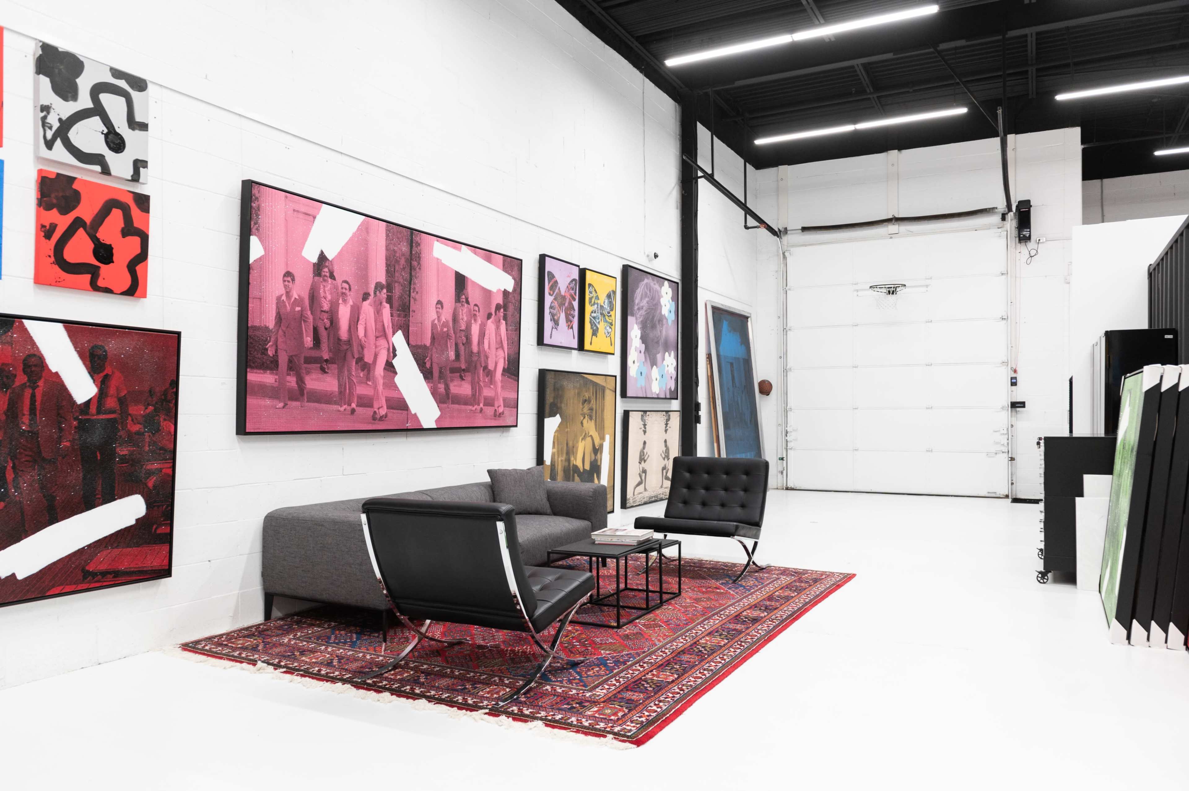 A spacious gallery with white walls featuring various framed artworks, a gray sofa, and a large area rug on a polished floor.