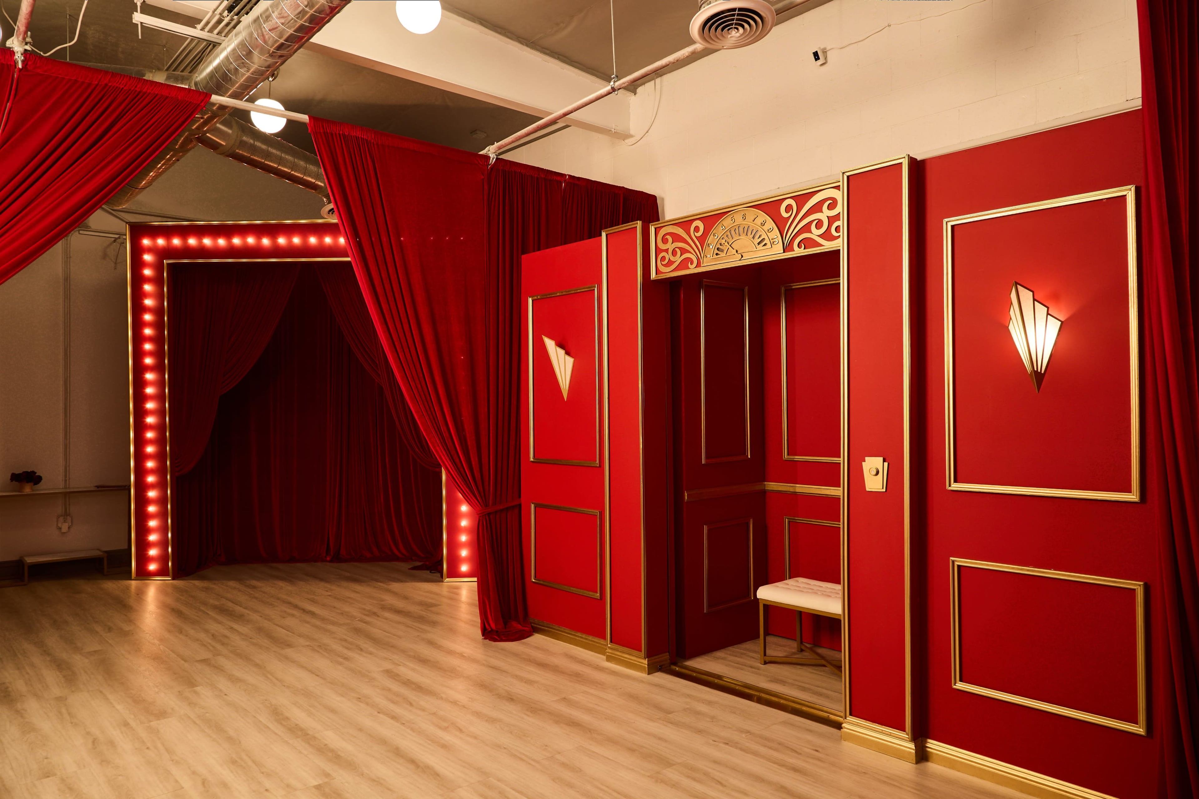 The image shows a vibrant red room featuring decorative curtains, wall sconces, and an ornate doorway with a bench.