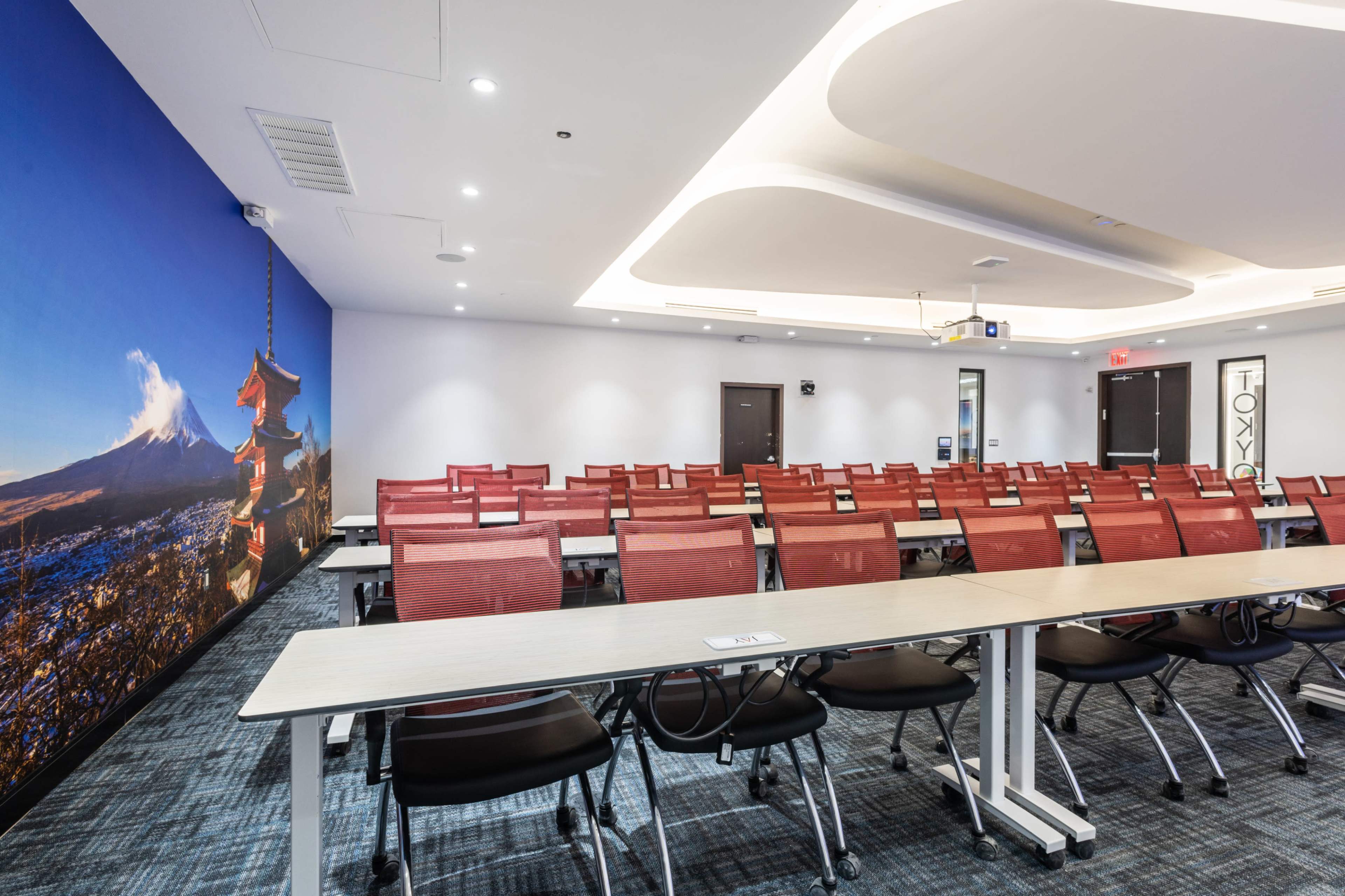 A conference room features rows of red chairs facing long tables, with a large mural of Mount Fuji on one wall.