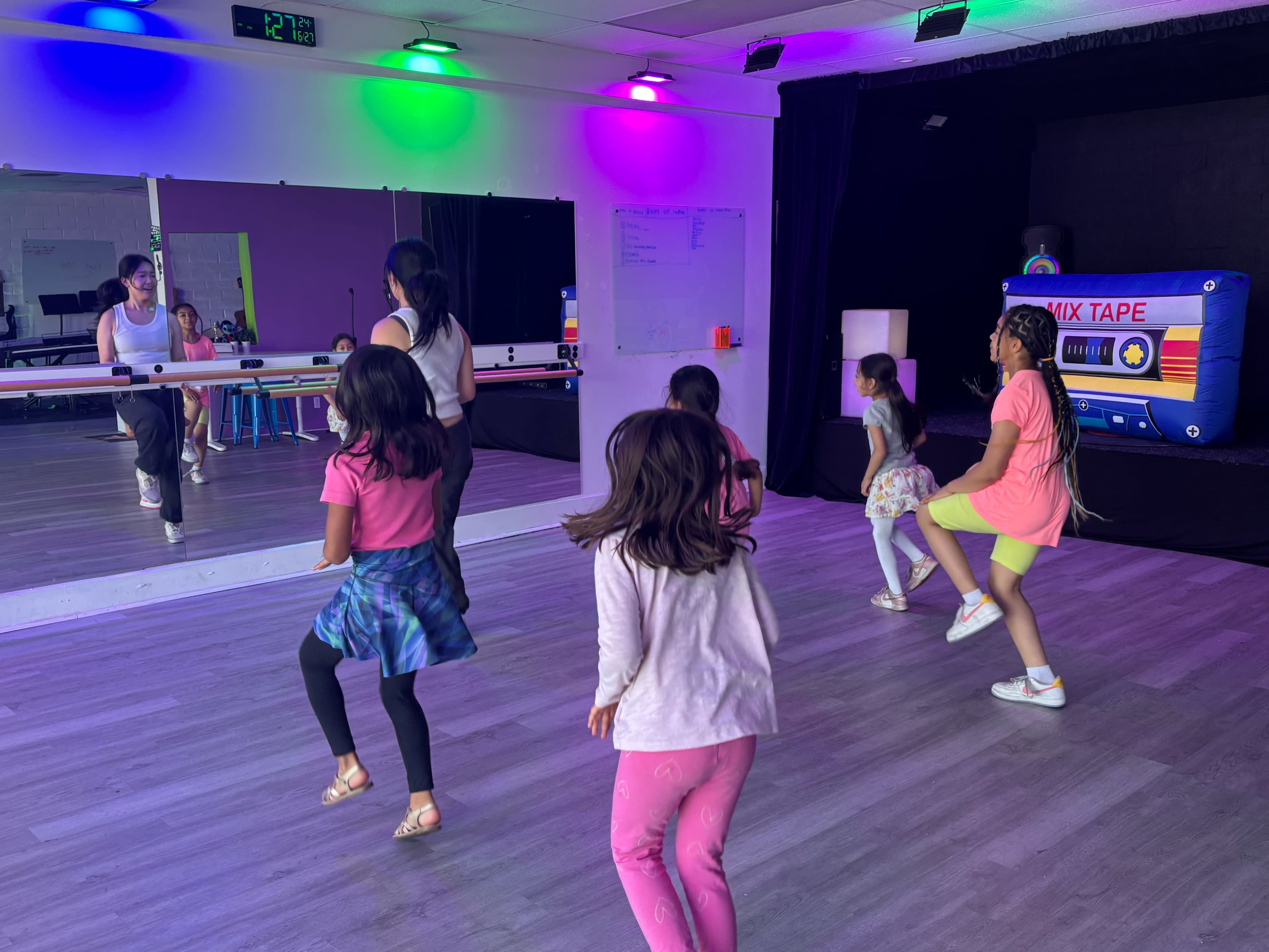 A group of children is dancing in a brightly lit studio with mirrors and colorful lights.