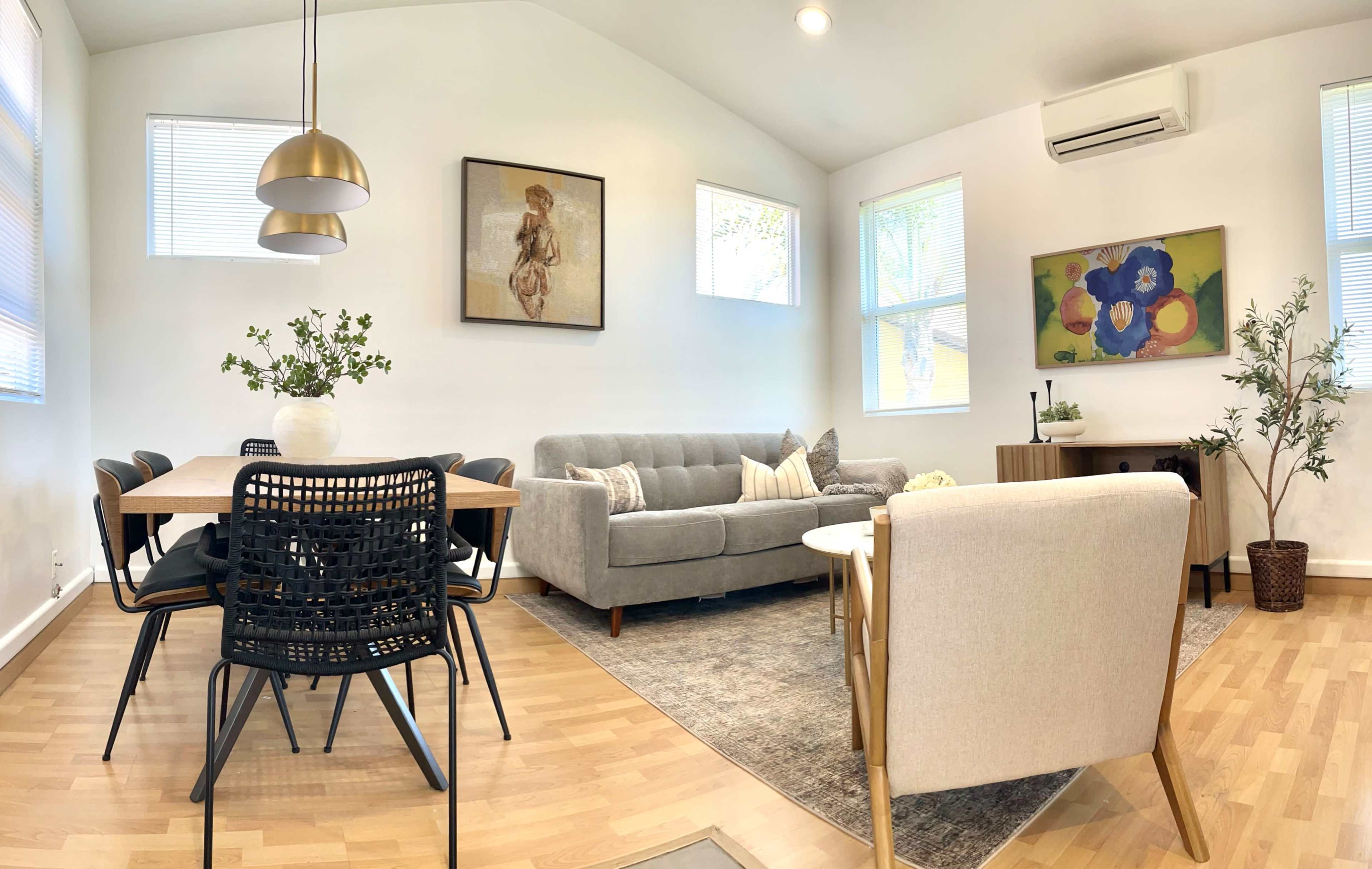A modern living area with a gray sofa, a dining table surrounded by black chairs, and artwork on the walls.