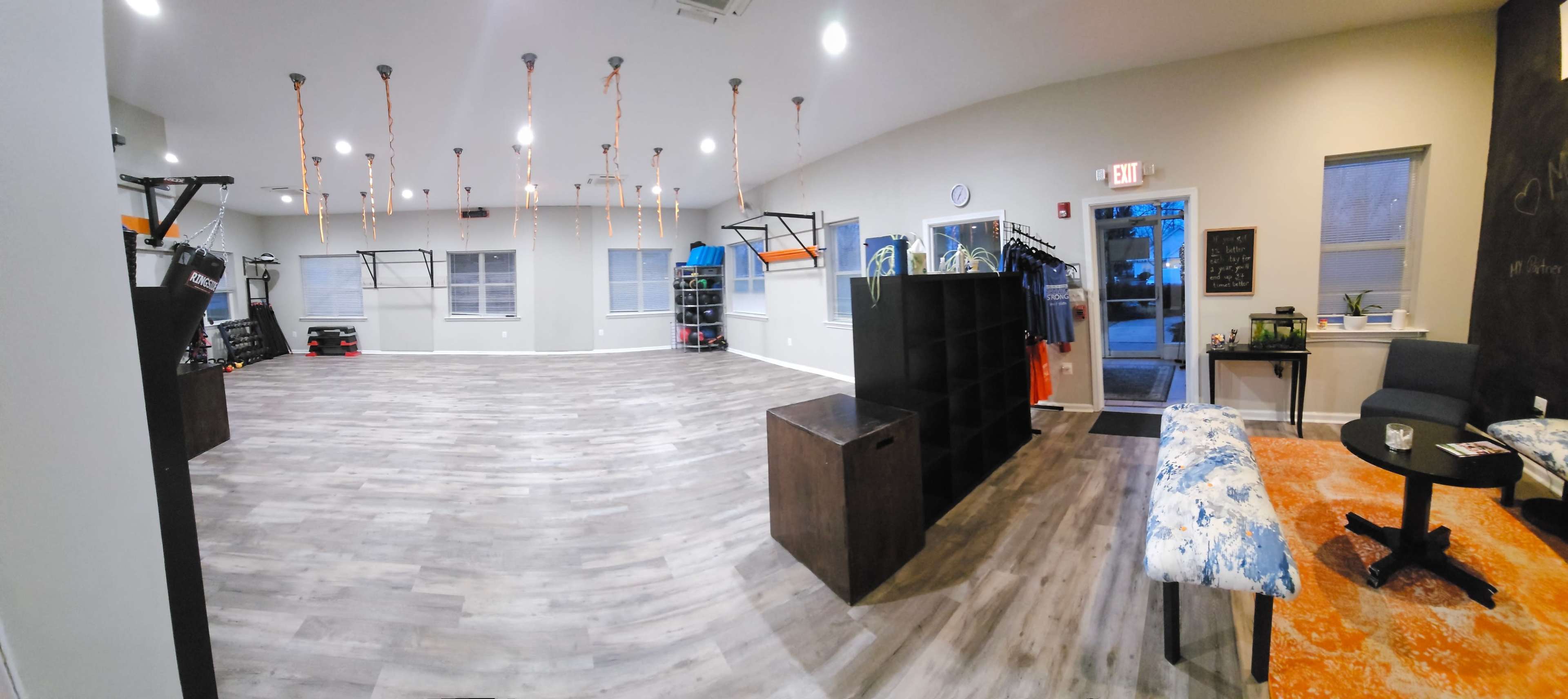 A spacious indoor area with wooden flooring, featuring workout equipment suspended from the ceiling and neatly organized shelving against the walls.