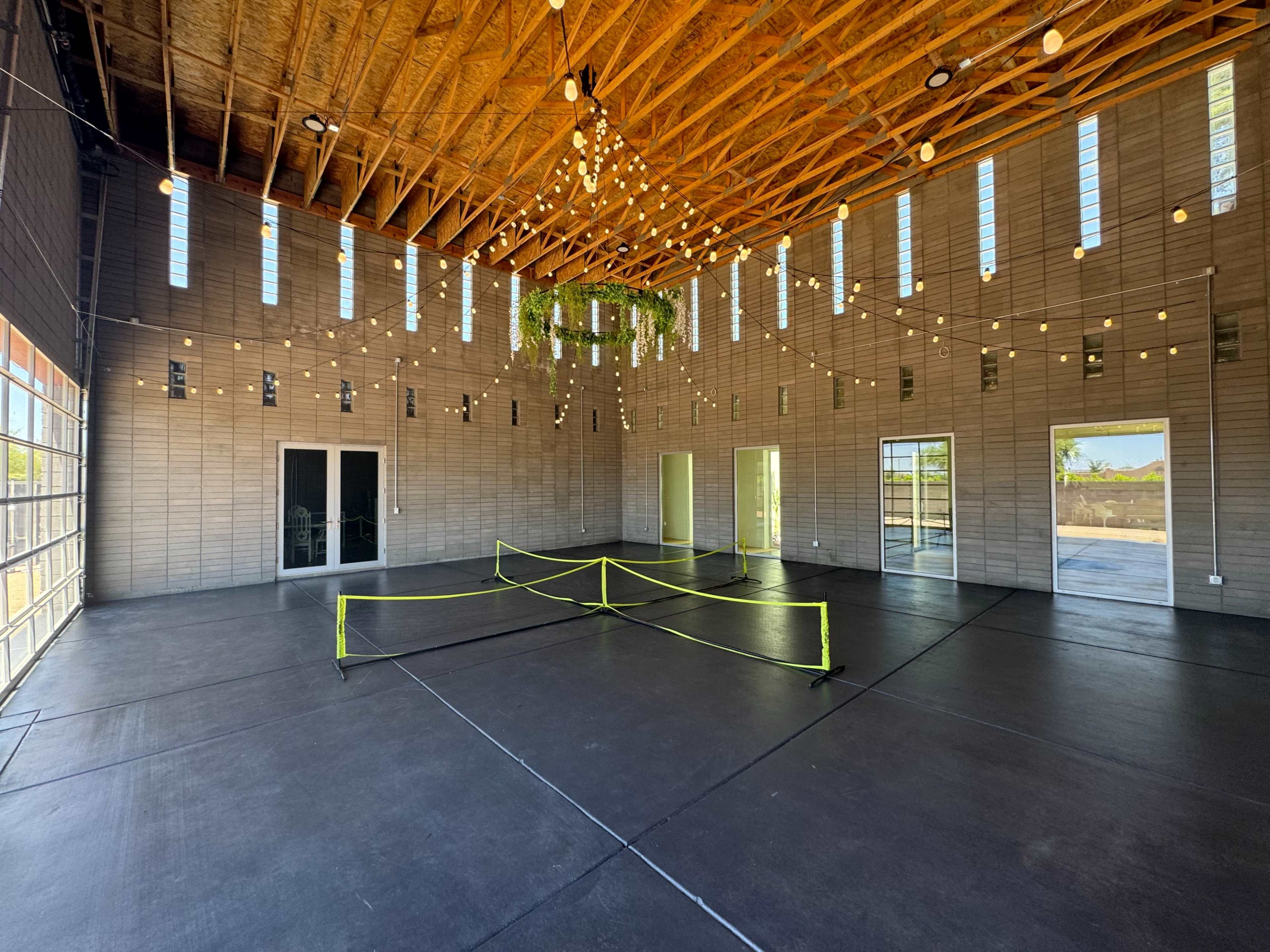 An interior space with high ceilings, large windows, and string lights, featuring a clear floor area marked by yellow caution tape.