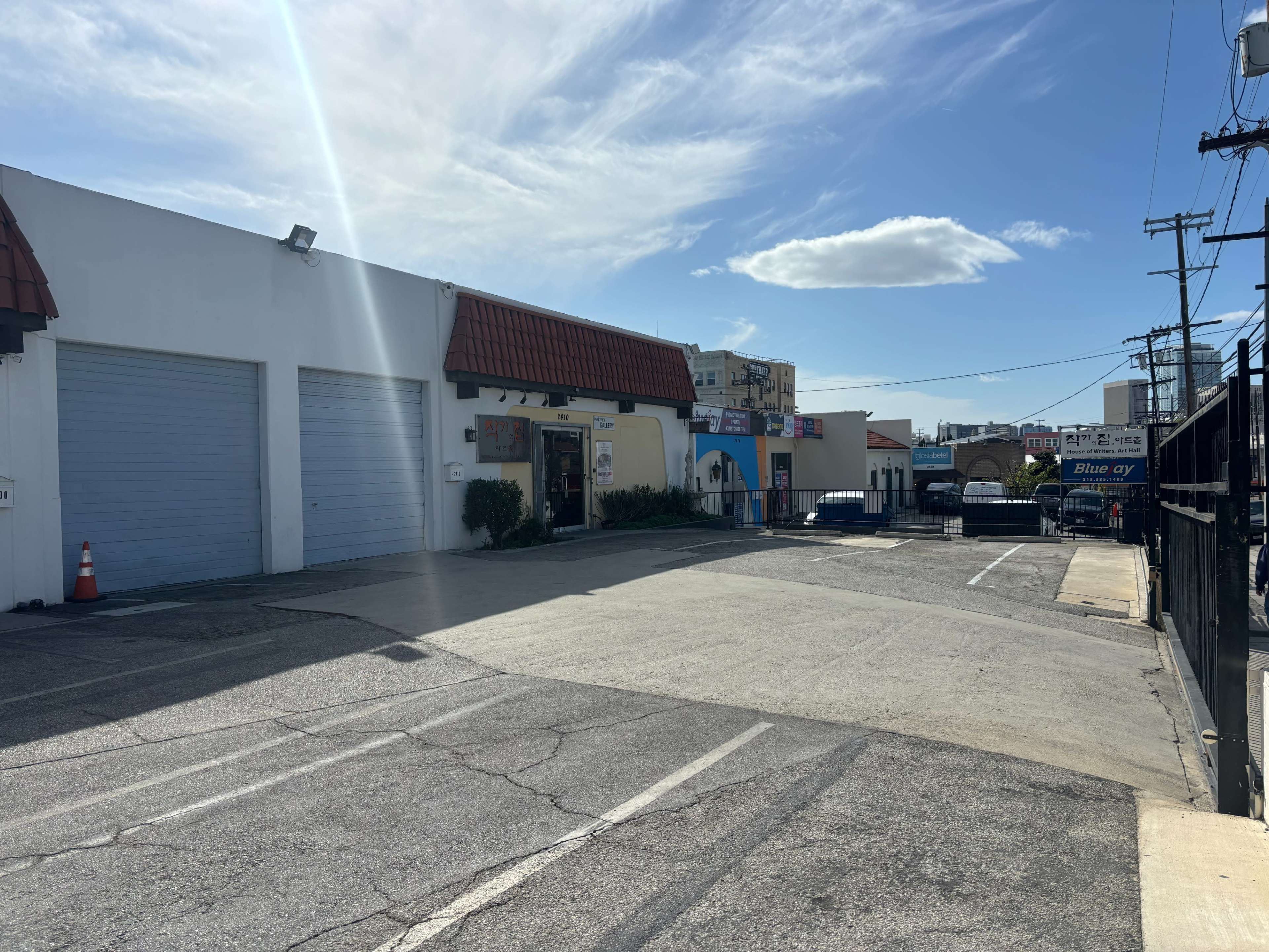 The image shows a parking lot next to a building with a red-tiled roof, featuring two closed garage doors and a clear blue sky overhead.