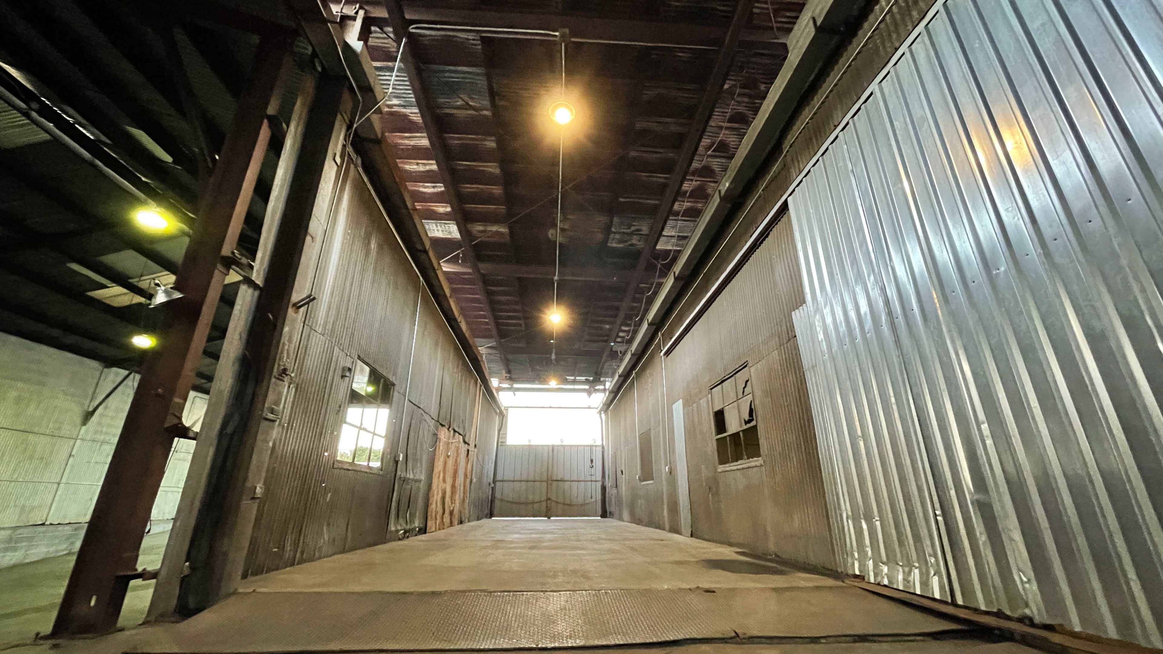 A long, industrial hallway with metal walls and overhead lights illuminating the space.