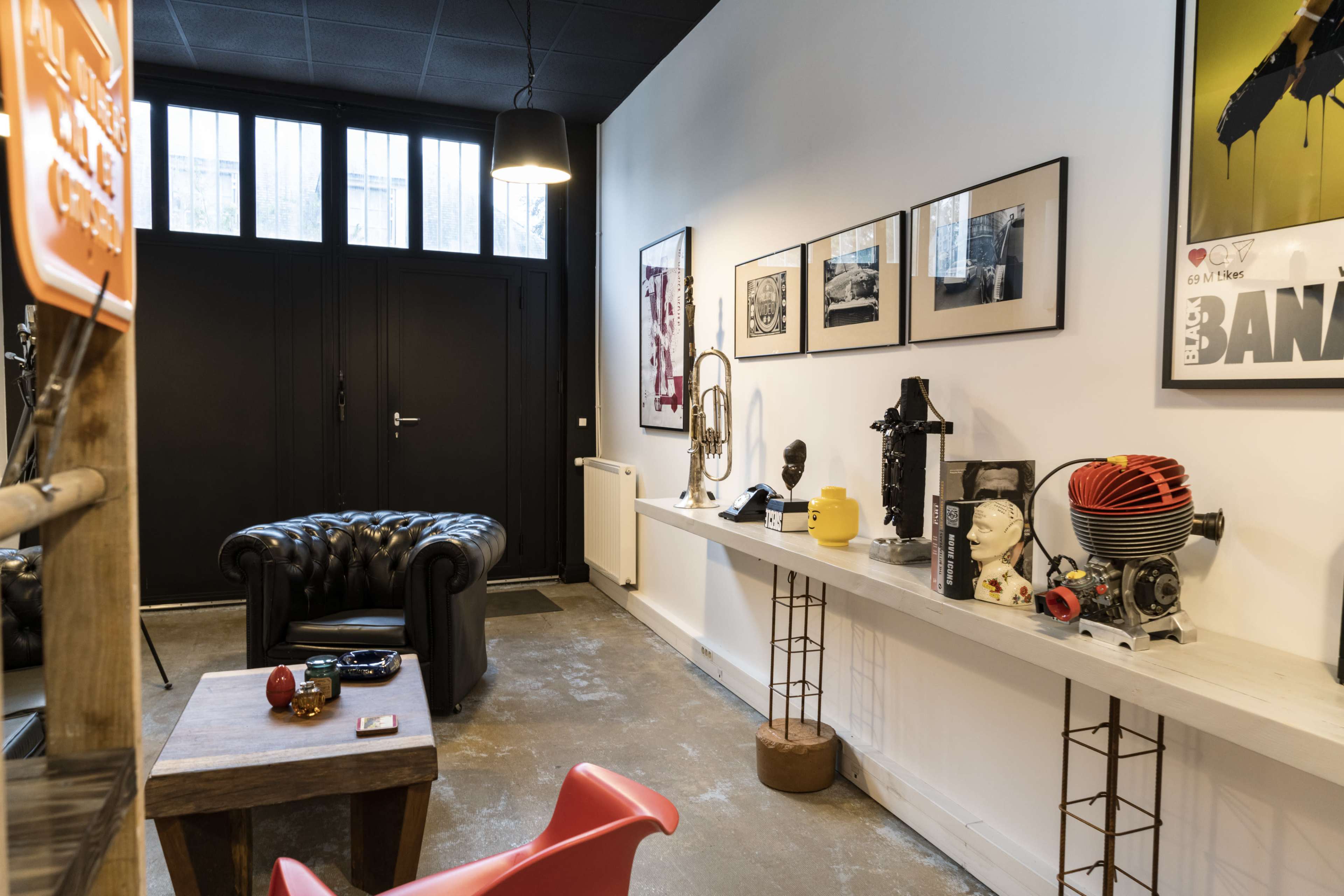 A stylish interior featuring a black leather chesterfield sofa, a wooden table, and a wall adorned with framed artworks and various decorative items.