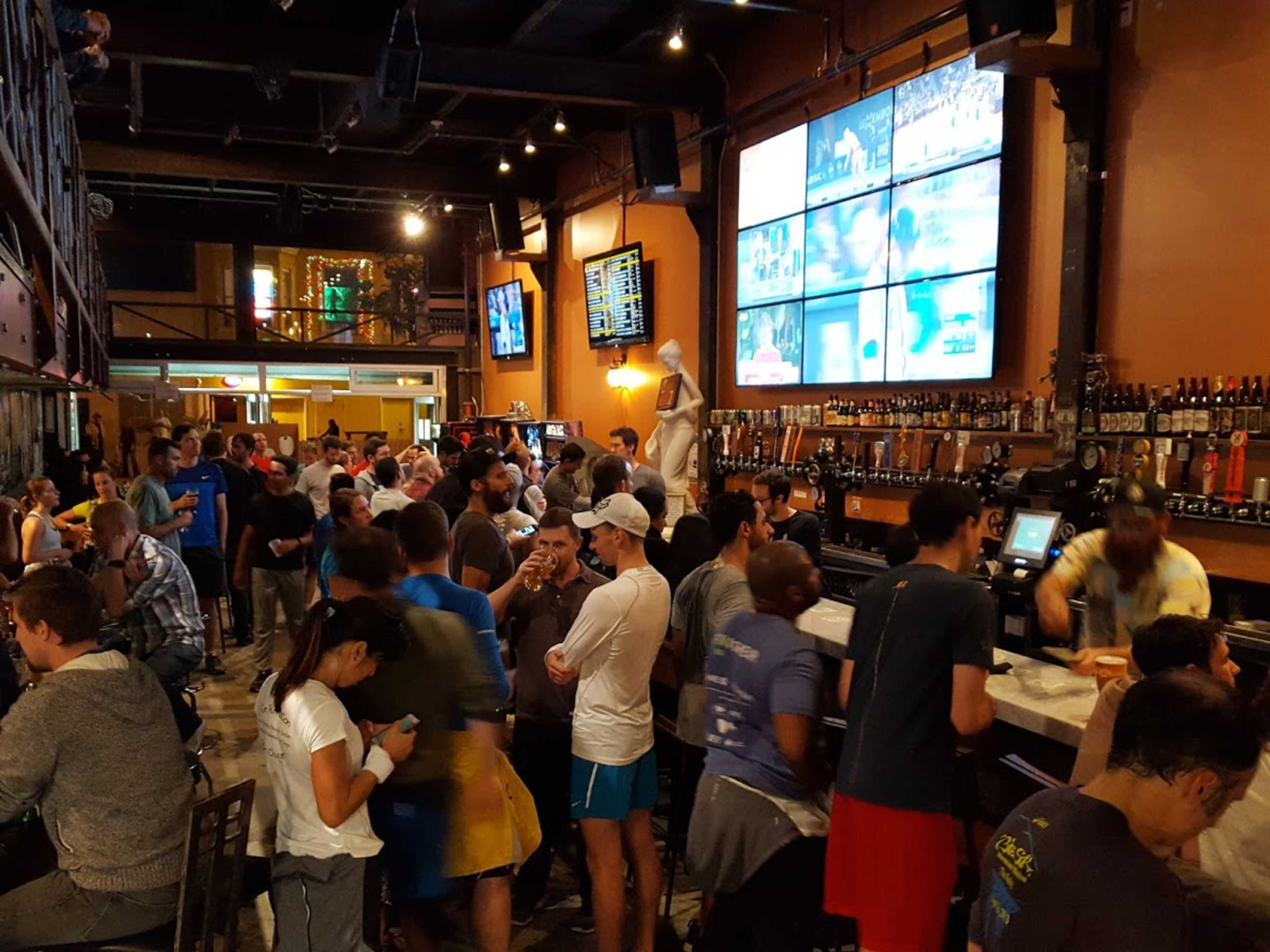 A crowded sports bar features many patrons socializing and watching games on multiple screens.