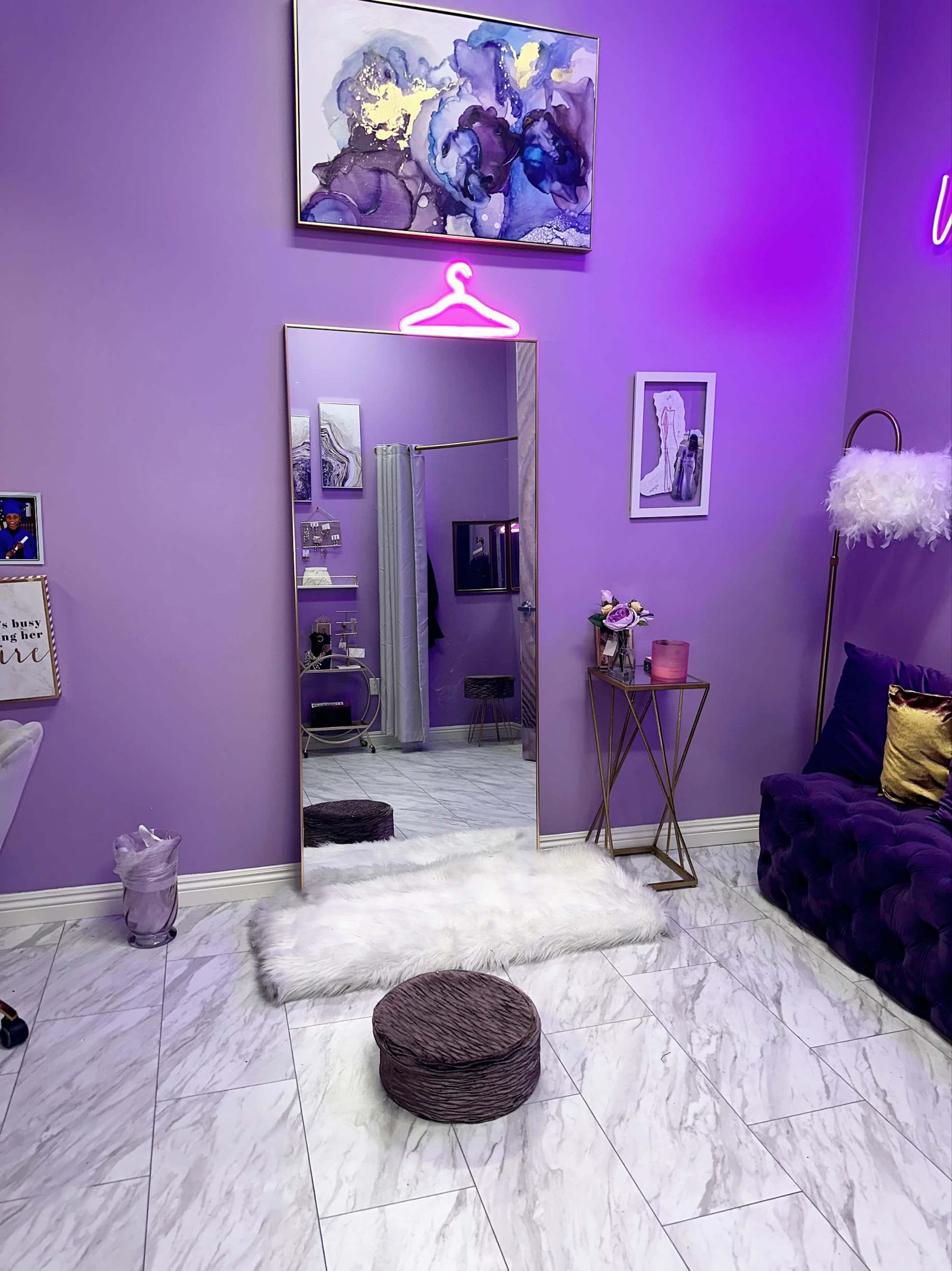 A stylish room with purple walls, a large mirror on the floor, a plush round ottoman, and decorative wall art, including a colorful painting.