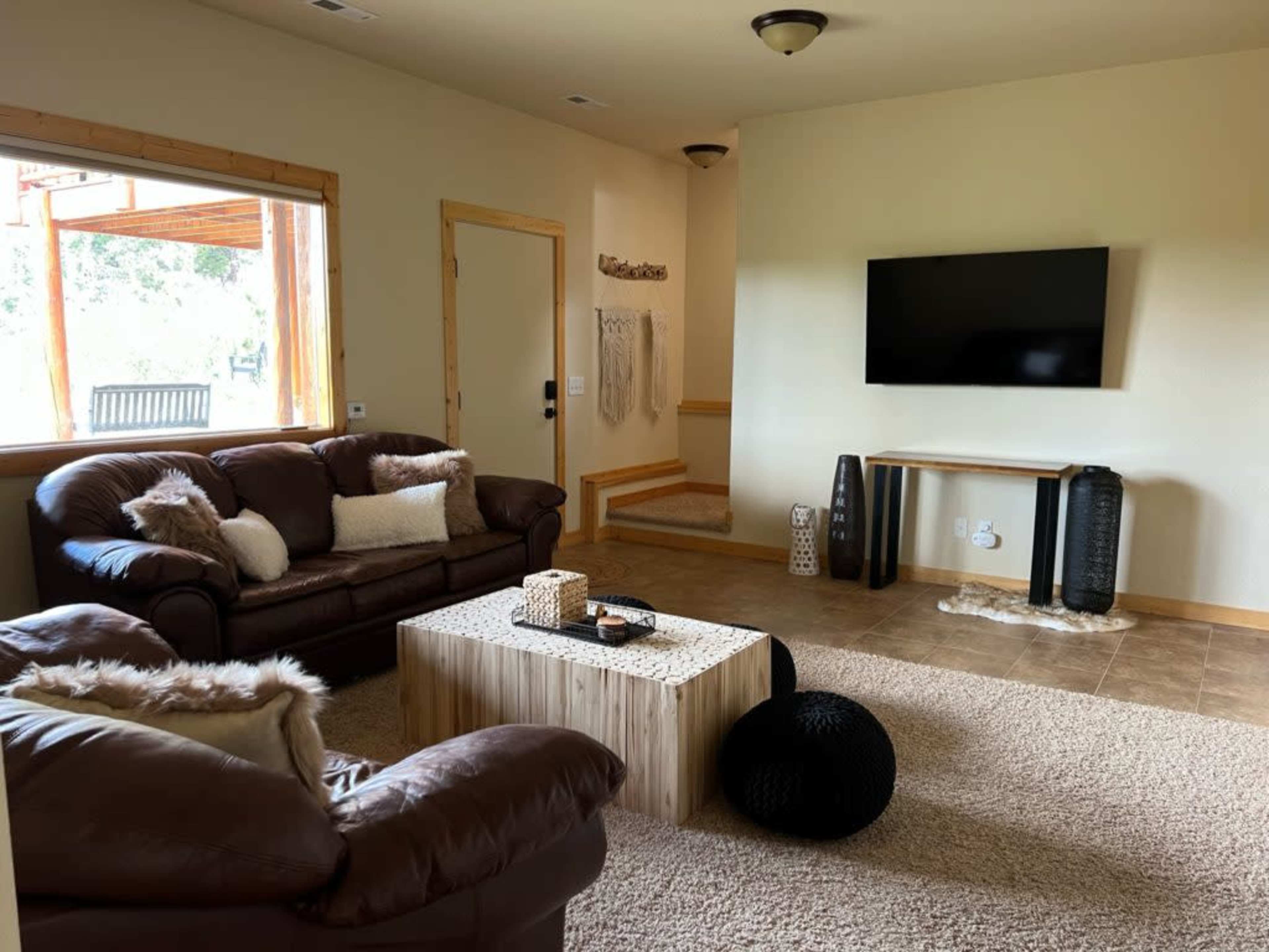The image shows a living room with brown leather sofas, a wooden coffee table, a television mounted on the wall, and a beige carpet.