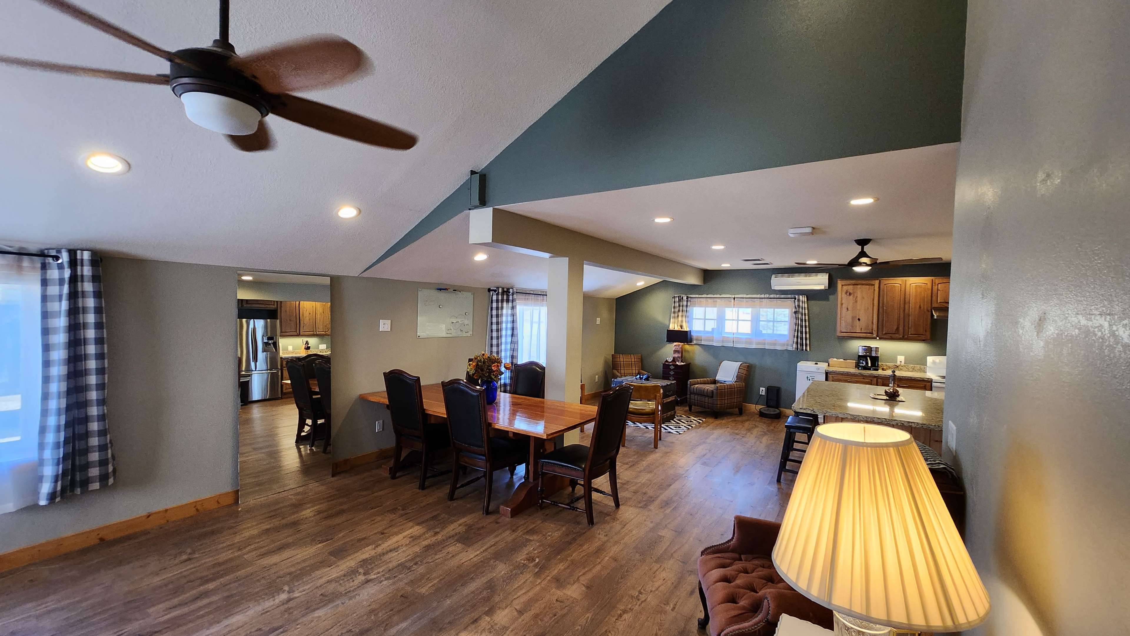 A modern open-concept living area with a dining table, kitchen, and cozy seating arrangement, featuring large windows and wooden flooring.