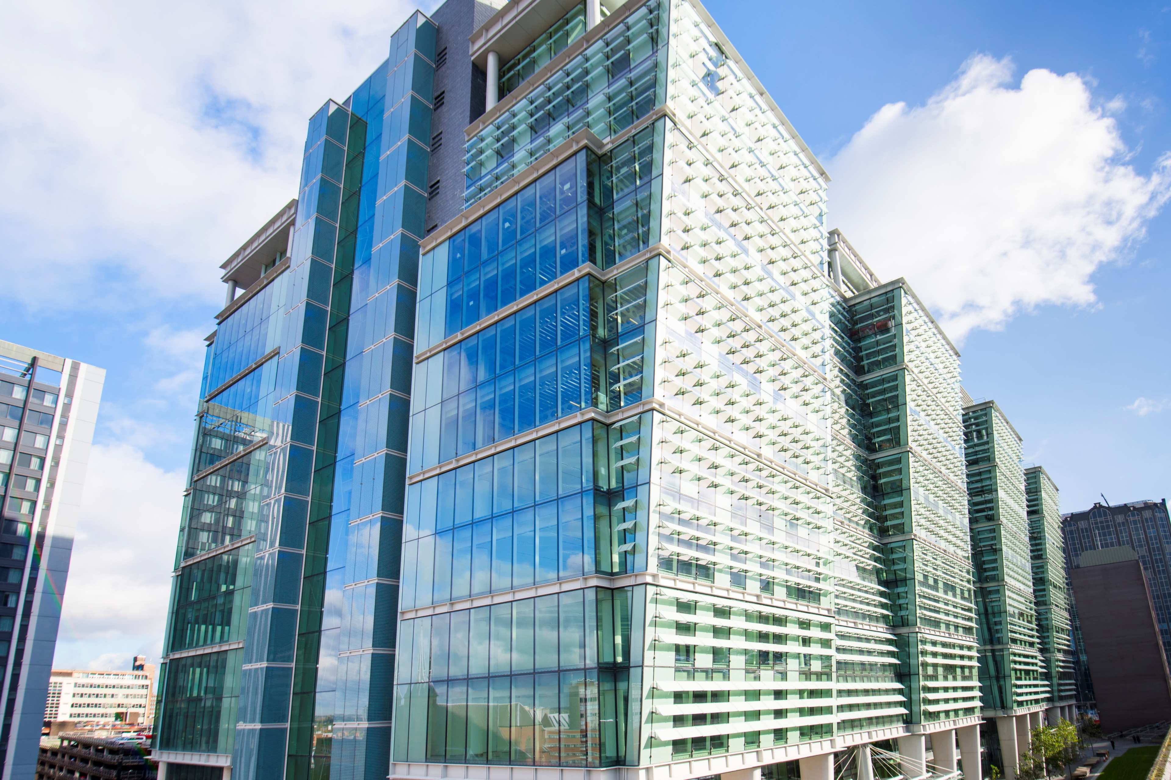 A modern glass office building features multiple stories with a reflective facade and a mix of green and blue tinted windows.