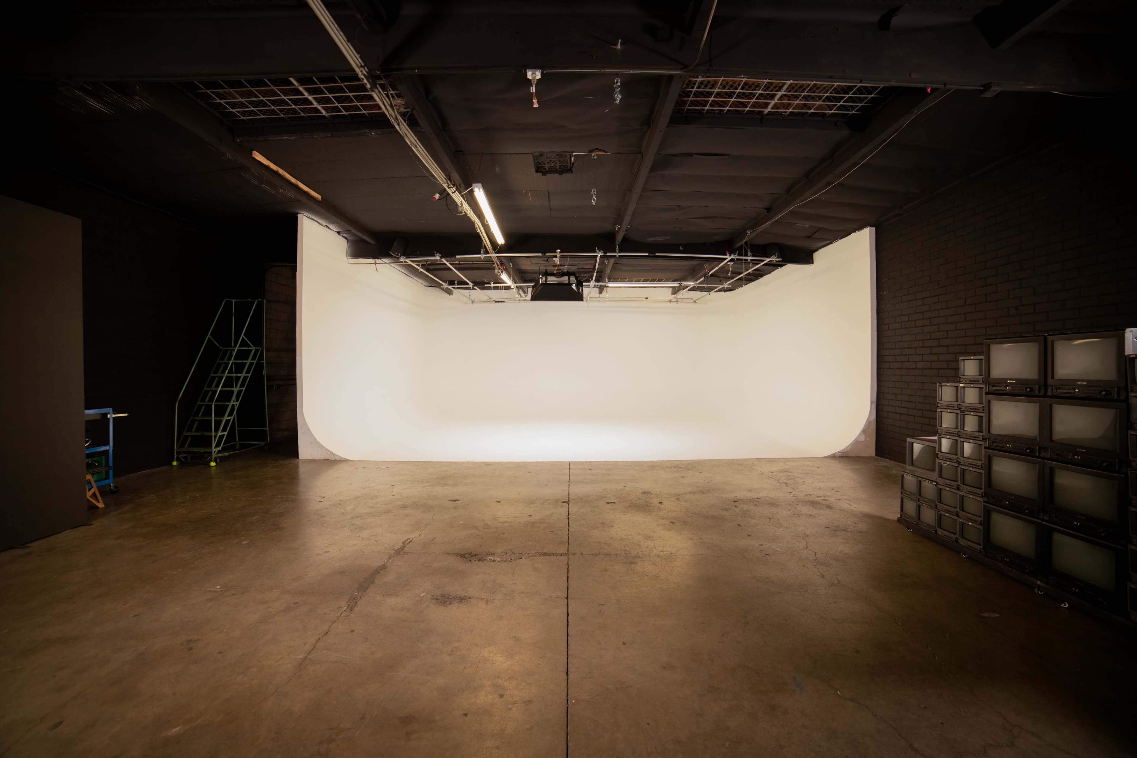 A spacious photo studio with a smooth white backdrop and concrete flooring, along with a stack of vintage televisions against one wall.