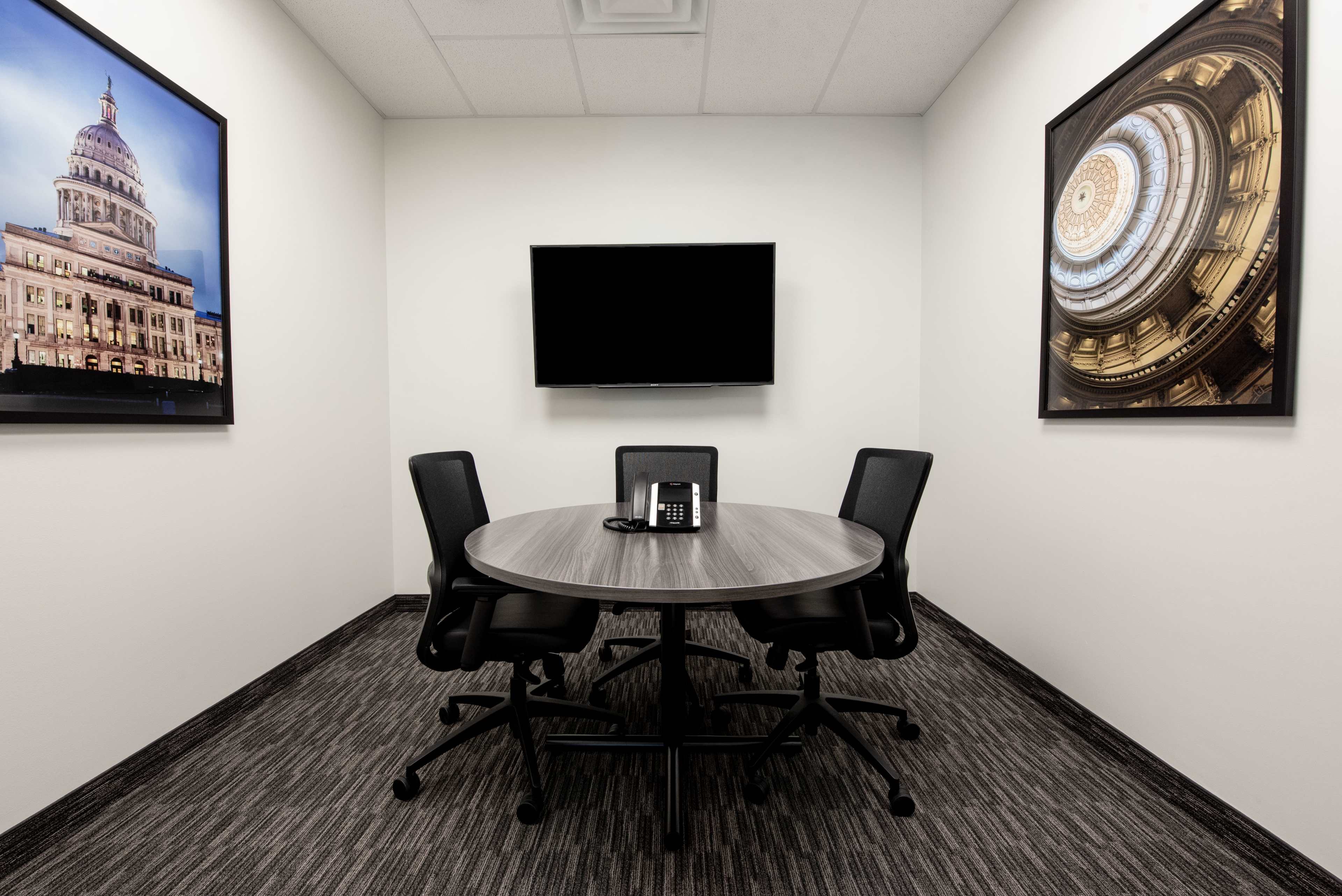 A small conference room features a round table with four chairs, a telephone, and two framed artworks on the walls.