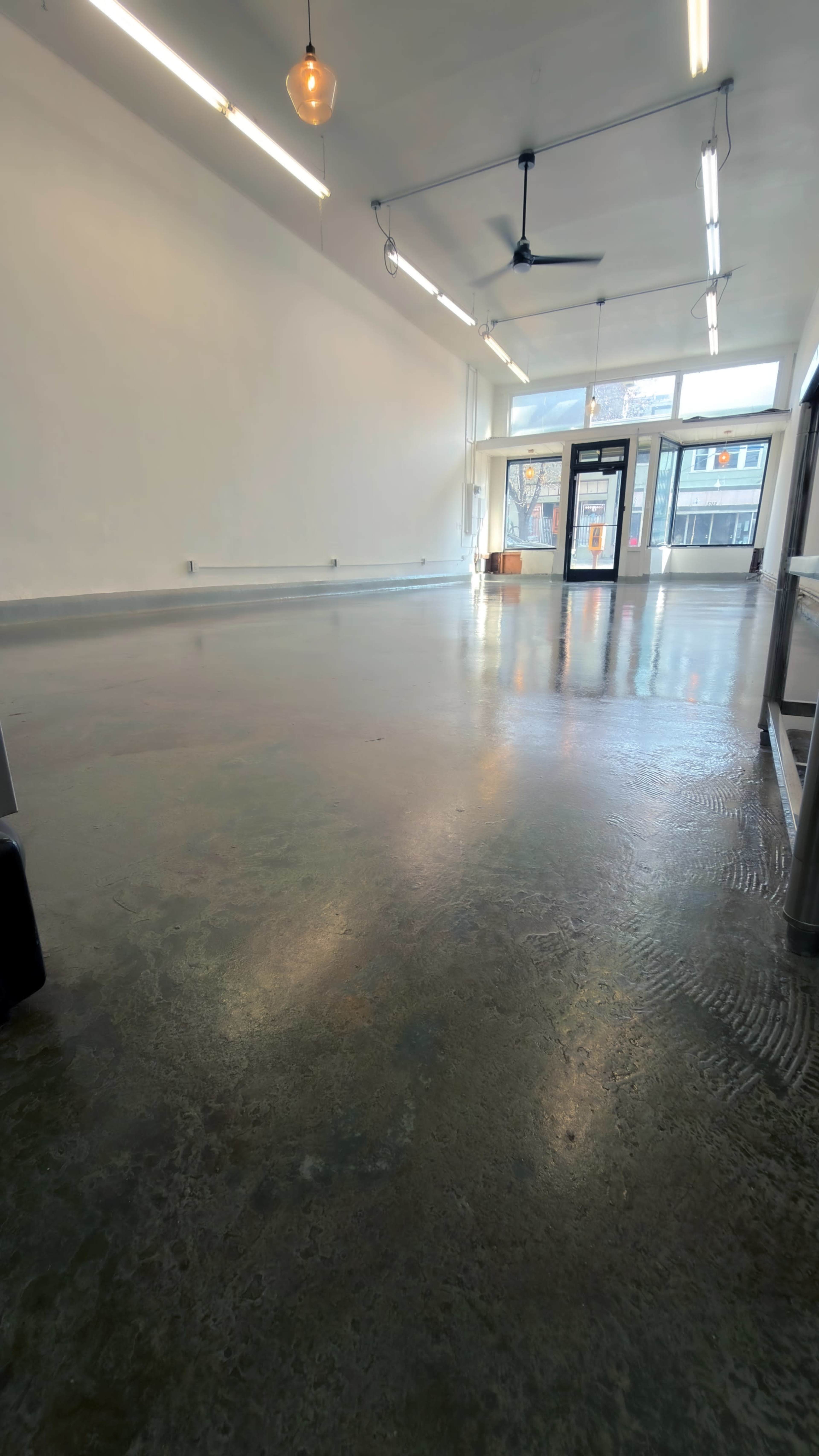 The image shows an empty interior space with a polished concrete floor and large windows at the entrance.