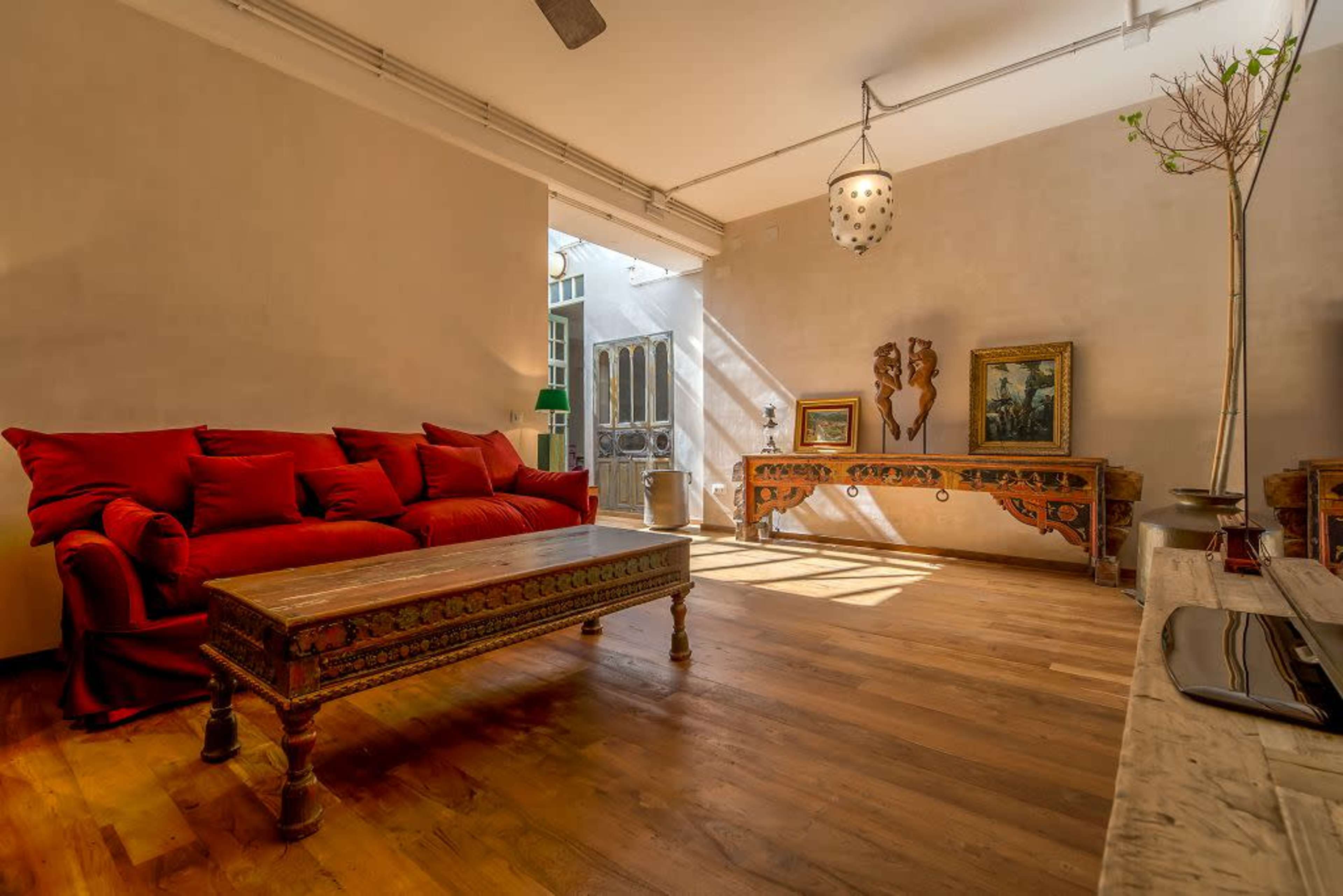 A bright, spacious room with a red sofa, a wooden coffee table, and decorative furniture along the walls.