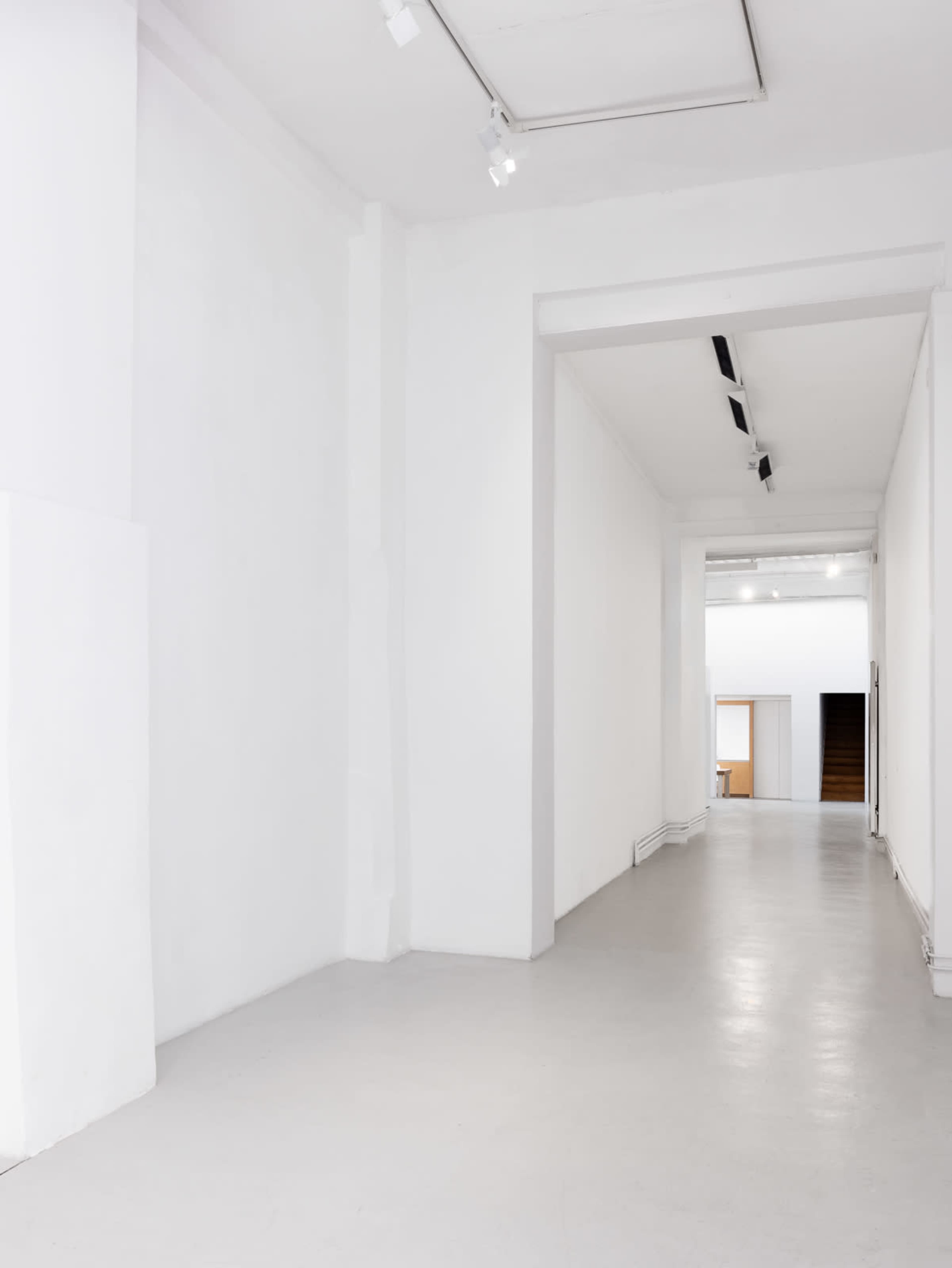The image shows a spacious, well-lit white hallway with minimalistic design and no visible decorations.