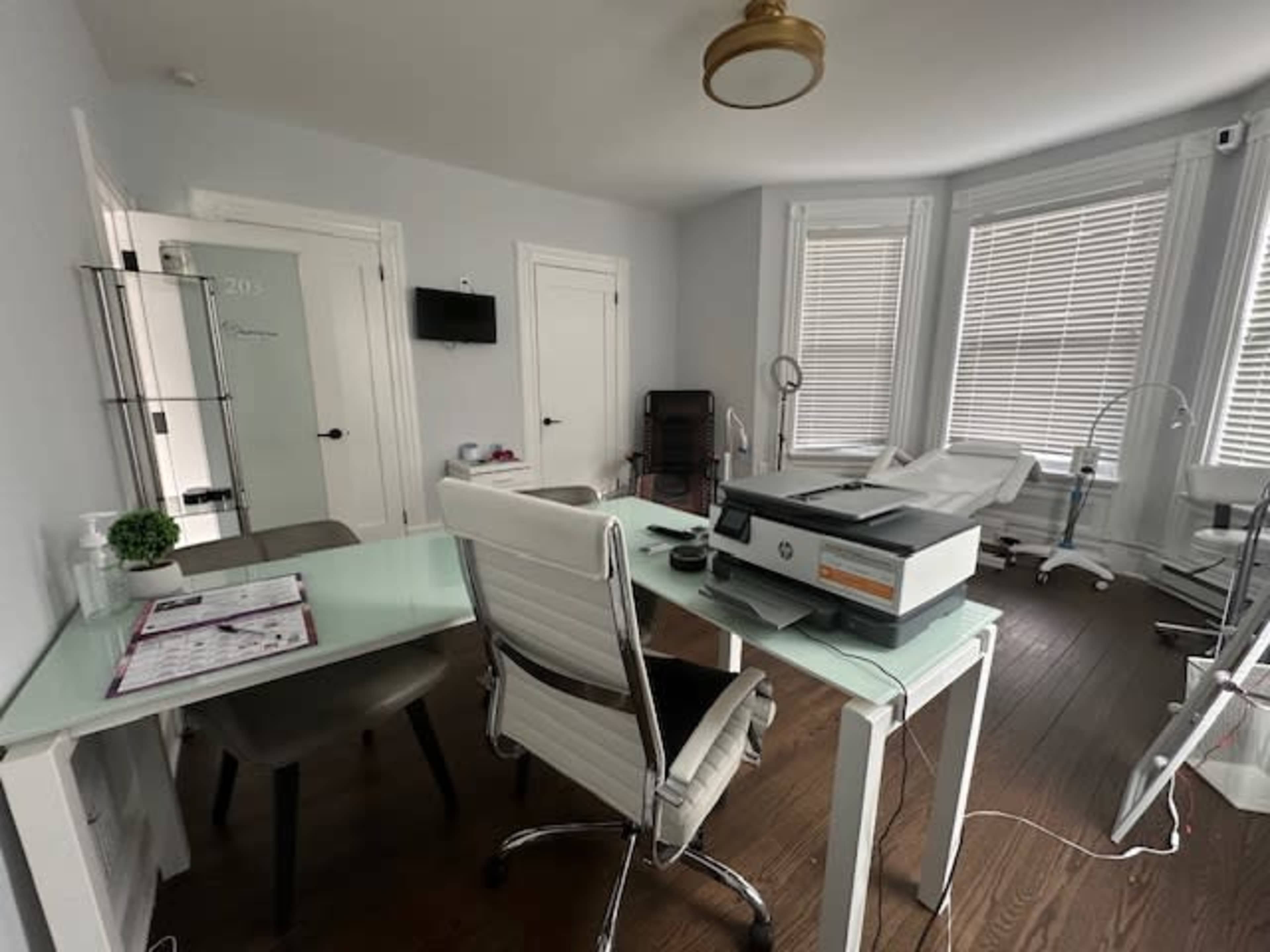 A well-lit office with a glass table, a printer, and several treatment chairs near large windows.