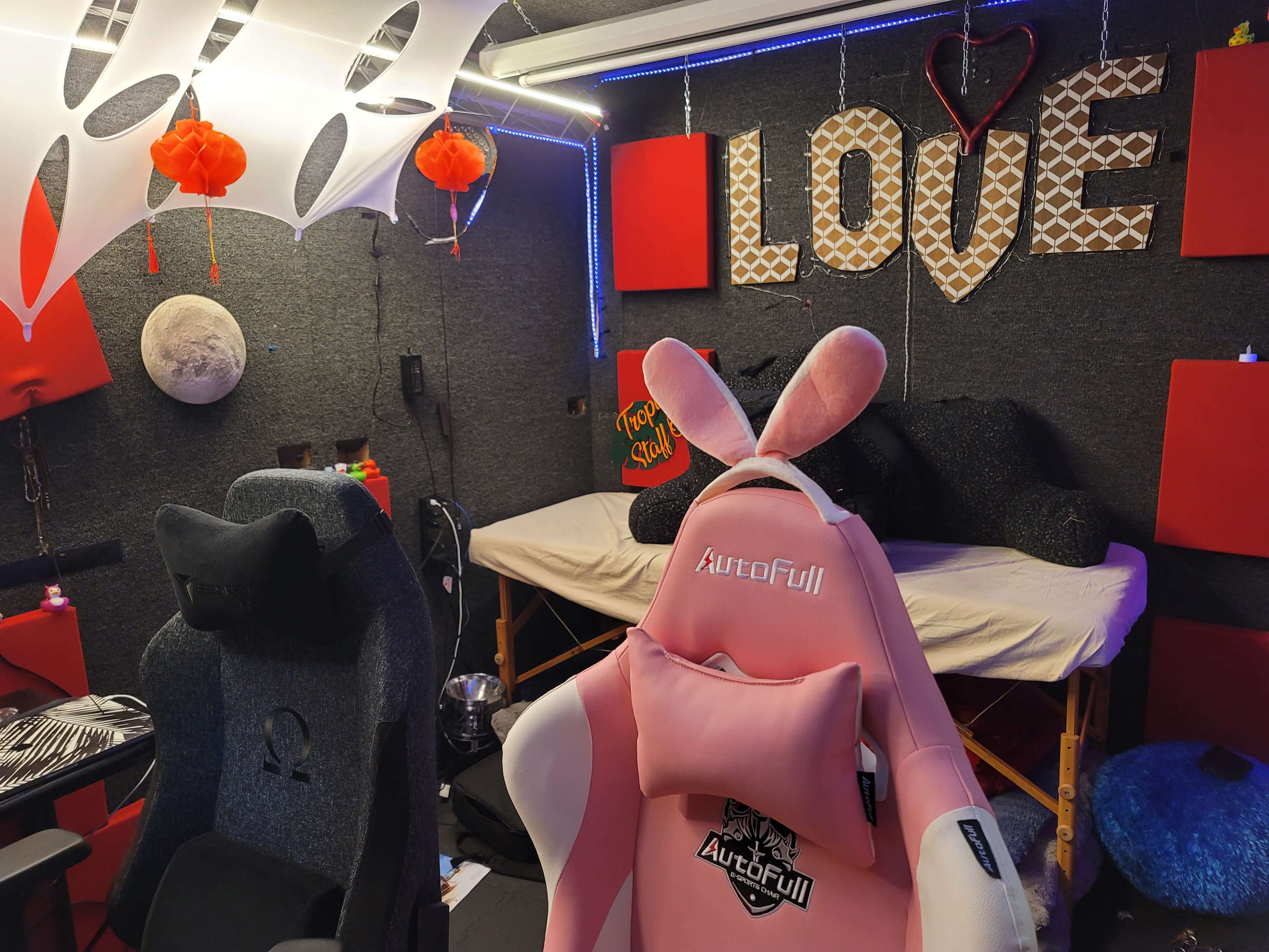 A small room with a pink gaming chair, decorative elements including a "LOVE" sign, and various colorful ornaments on the walls and ceiling.