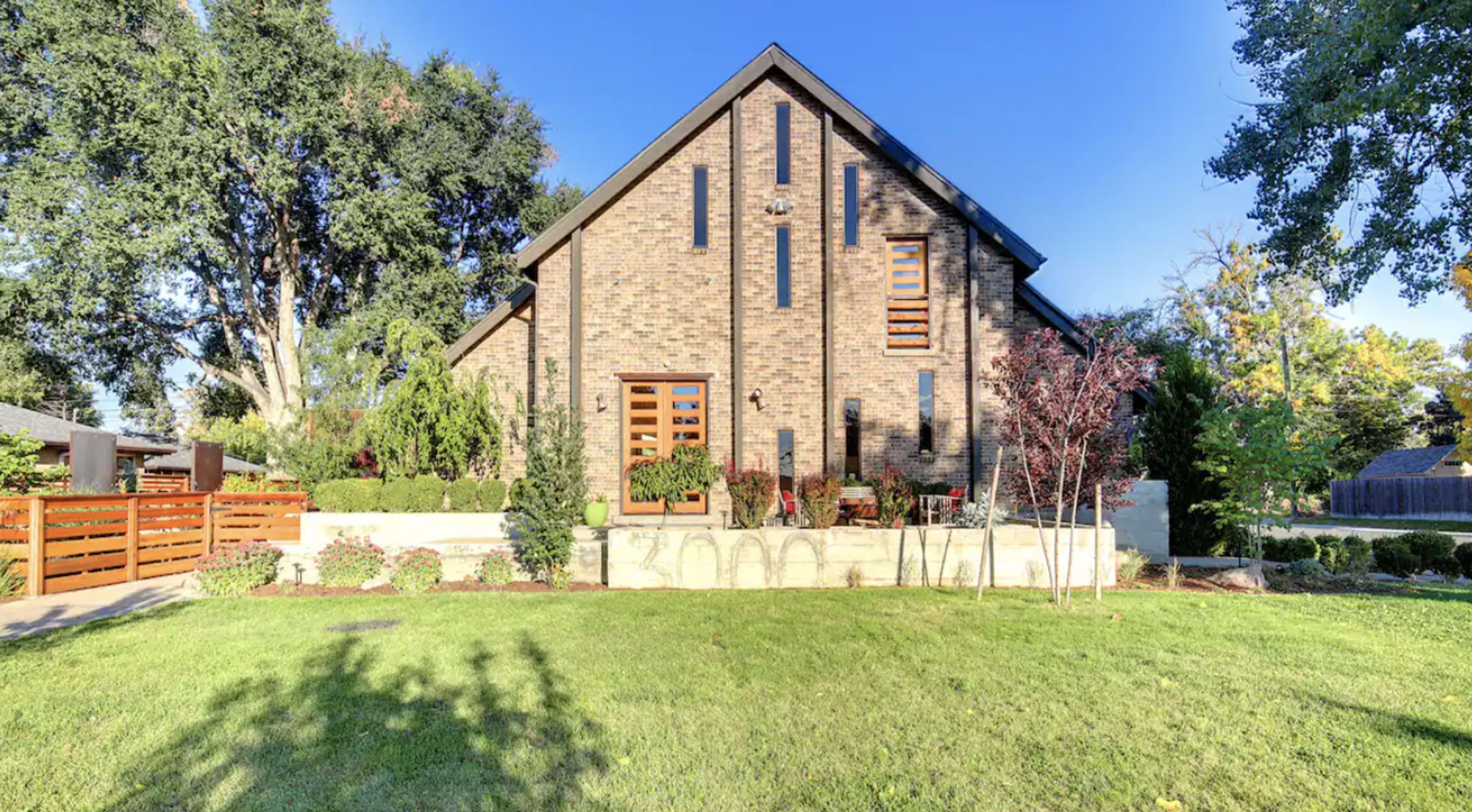 A two-story brick house with large windows and a landscaped front yard sits in a residential area.