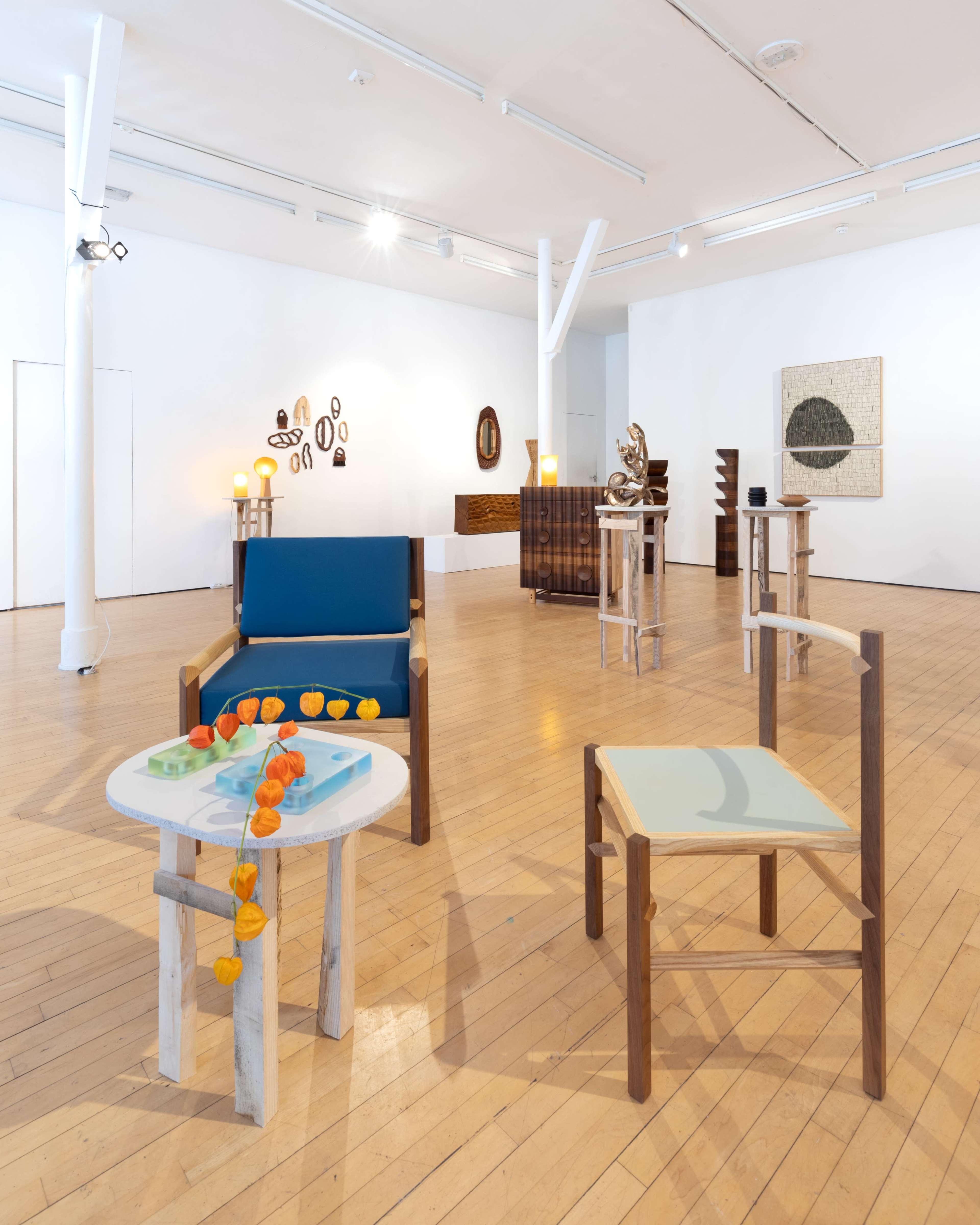 An art gallery featuring modern furniture and various artworks displayed on the walls, with wooden floors and bright lighting.