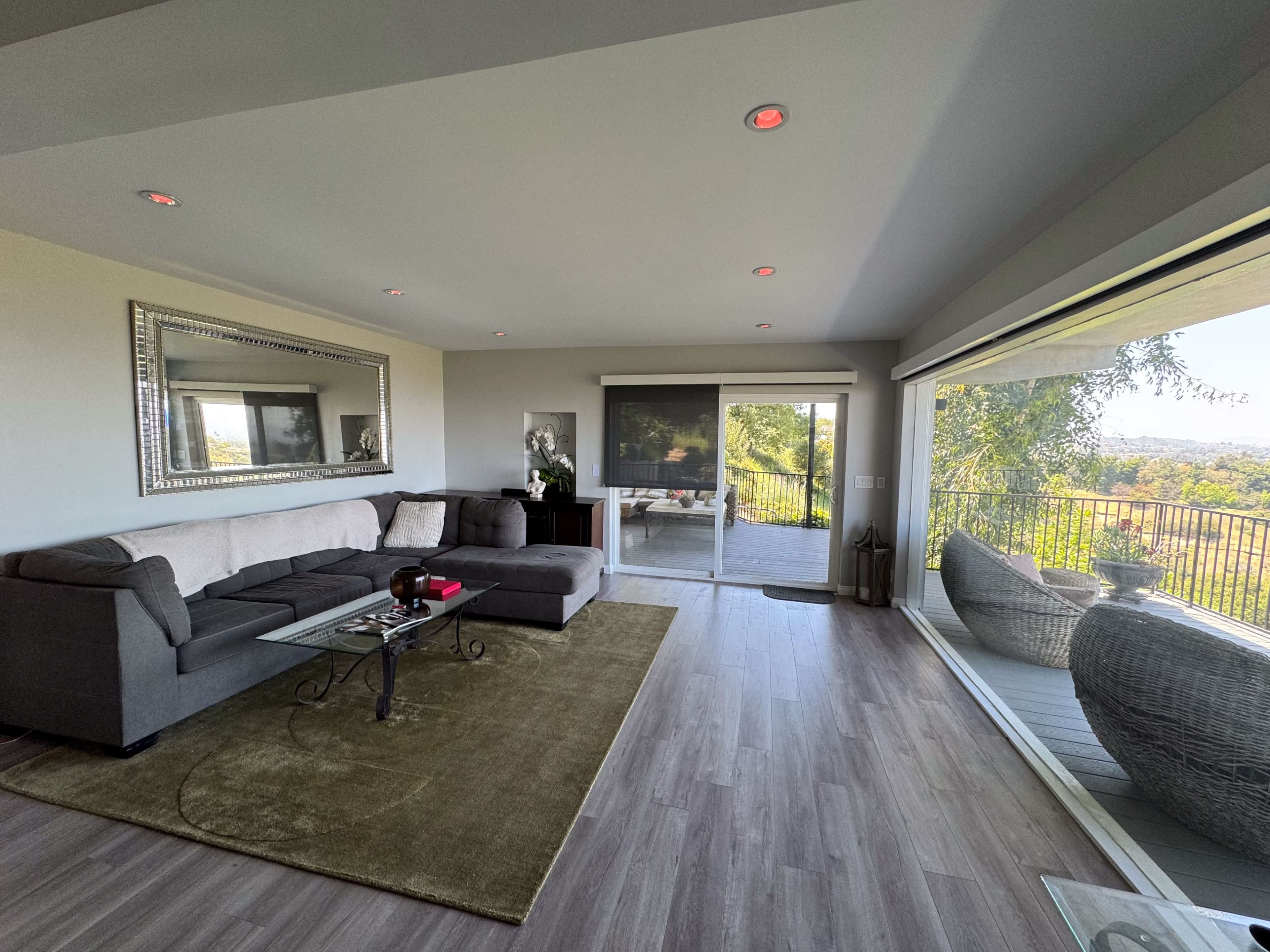 A modern living room with a gray sectional sofa, a glass coffee table, and large sliding doors that open to a balcony with a scenic view.