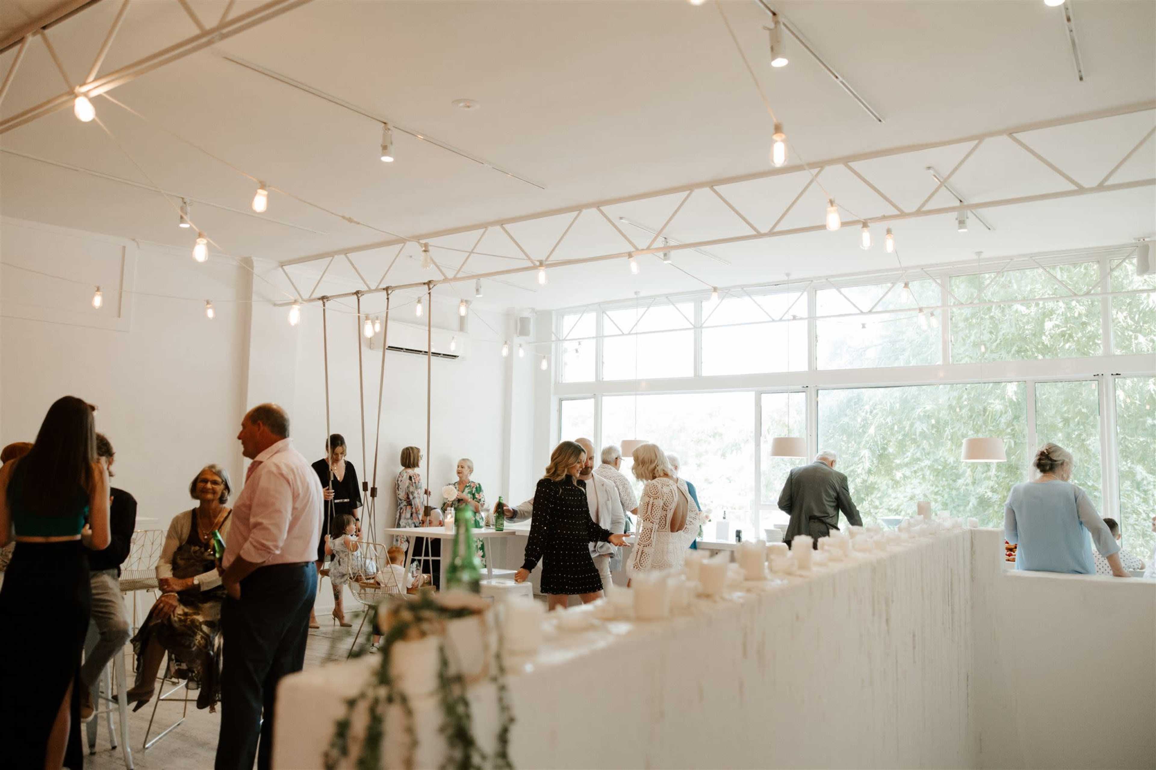 A group of people gathers in a bright, modern event space with large windows and decorative lighting.