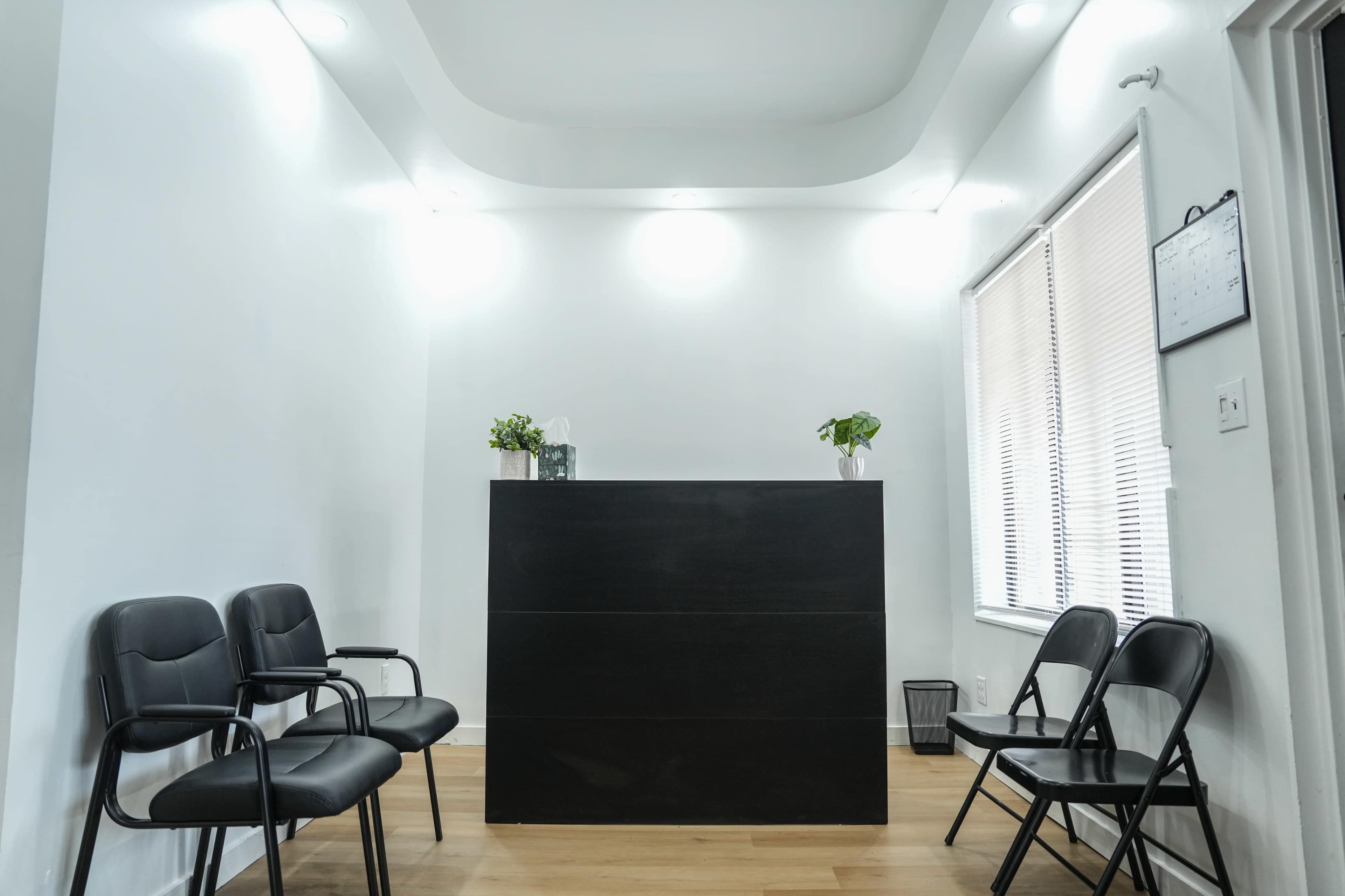 The image shows a minimalist reception area with a dark counter and several black chairs arranged around it.