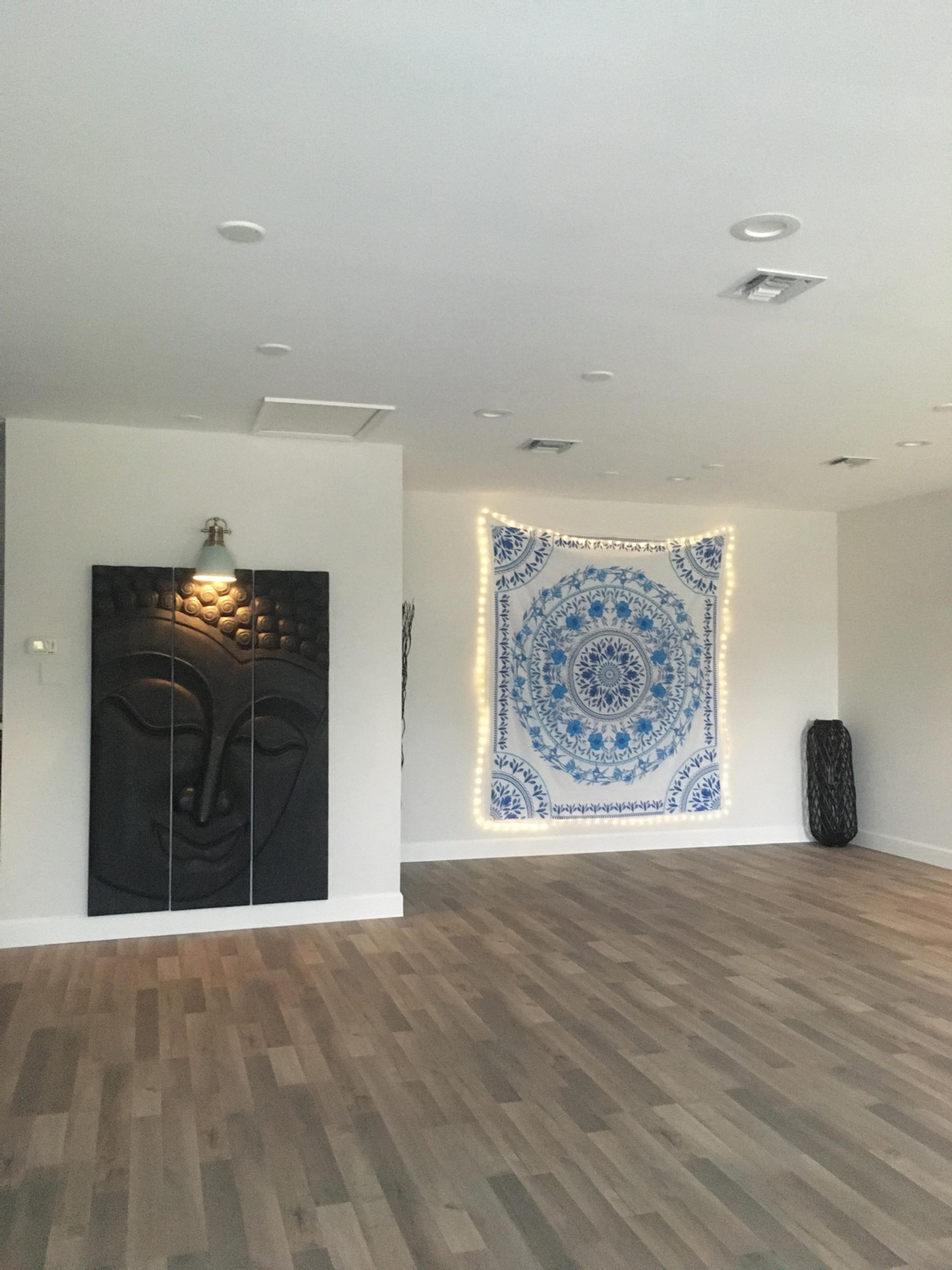 A spacious room with wooden flooring, featuring a wall tapestry and a large decorative wall panel with a Buddha face.