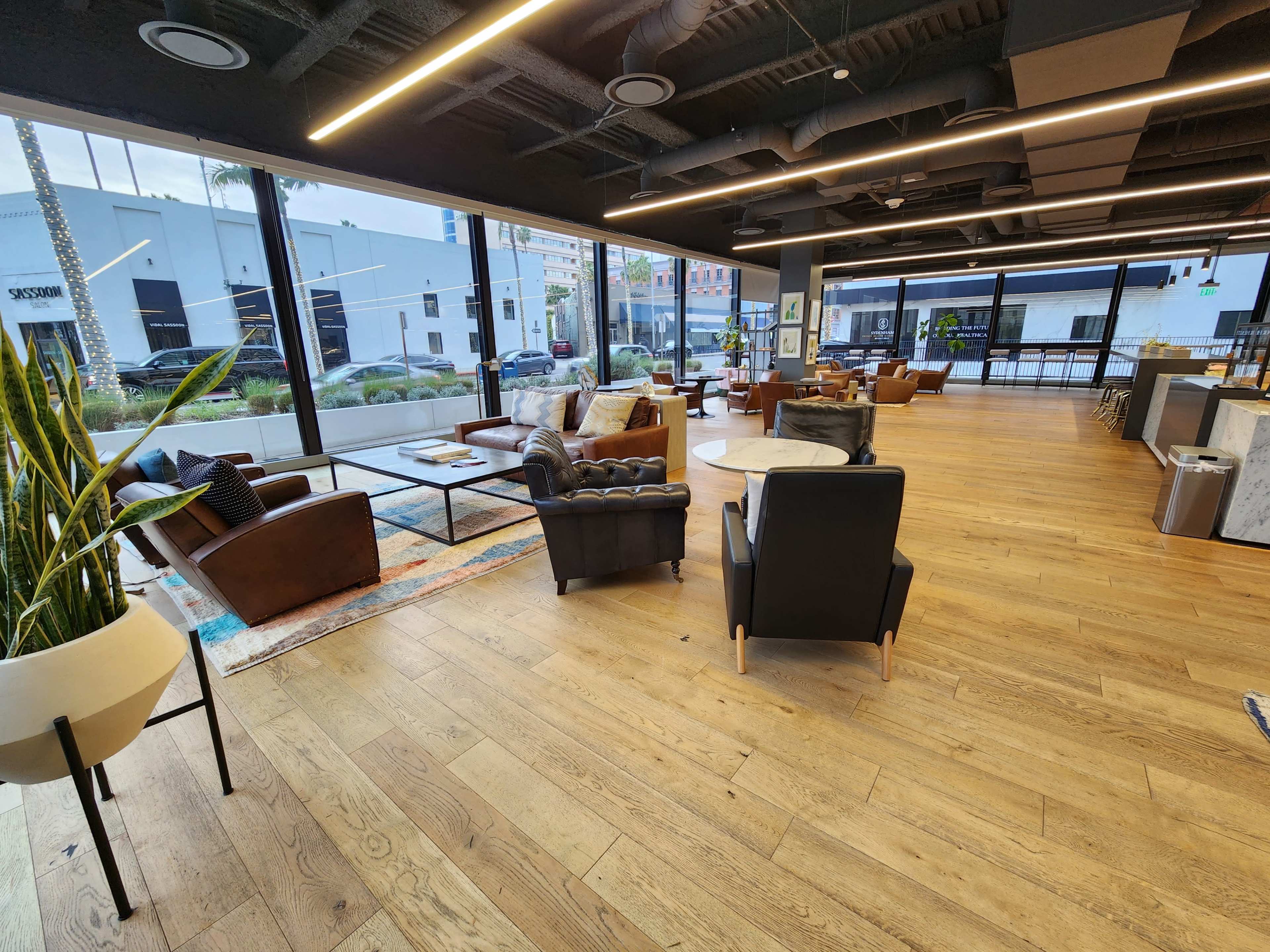 A spacious, modern cafe with wooden flooring, large windows, and various seating arrangements including leather chairs and a coffee table.