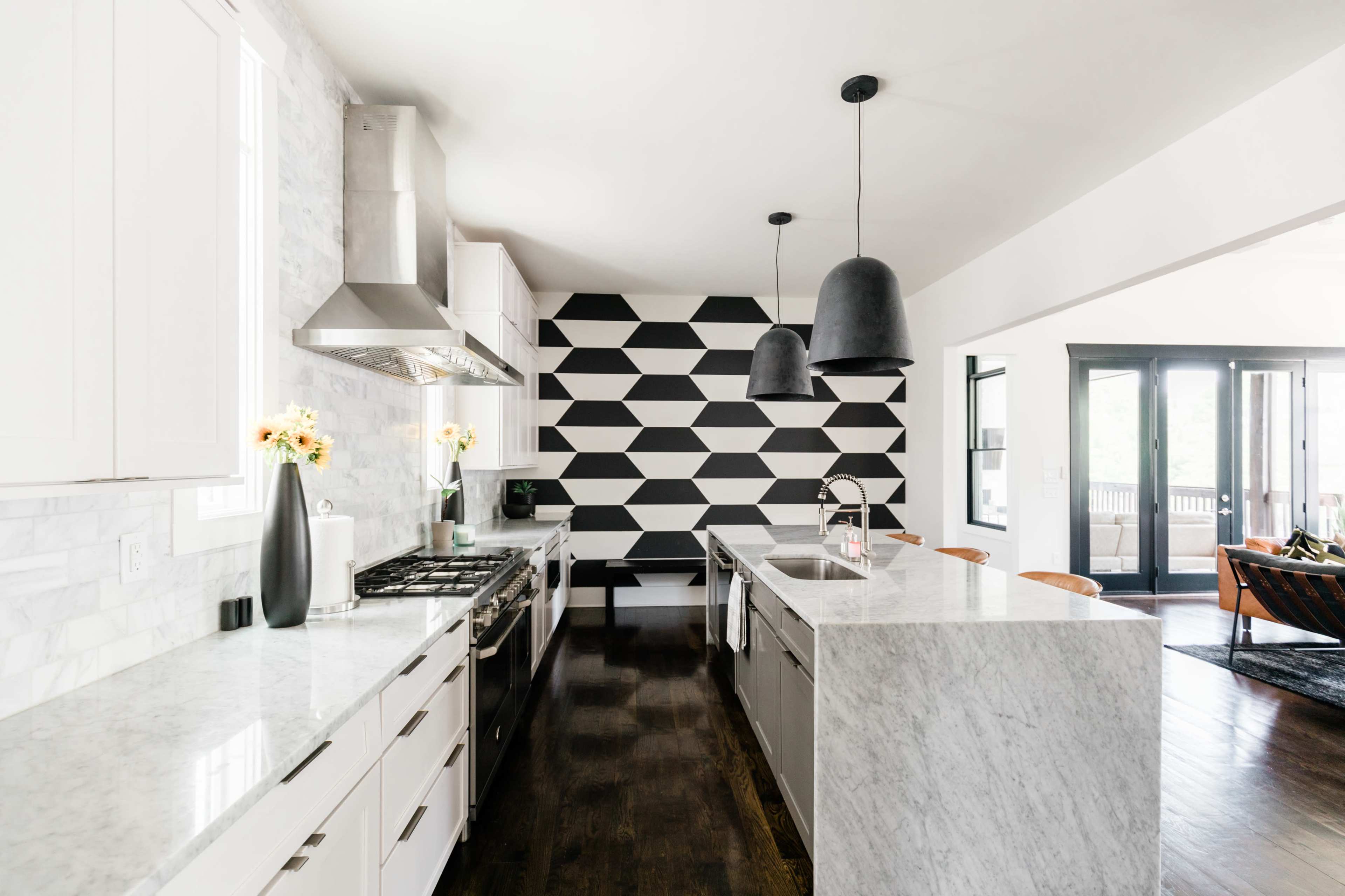 A modern kitchen features a large marble island, sleek cabinetry, and a black and white geometric accent wall.
