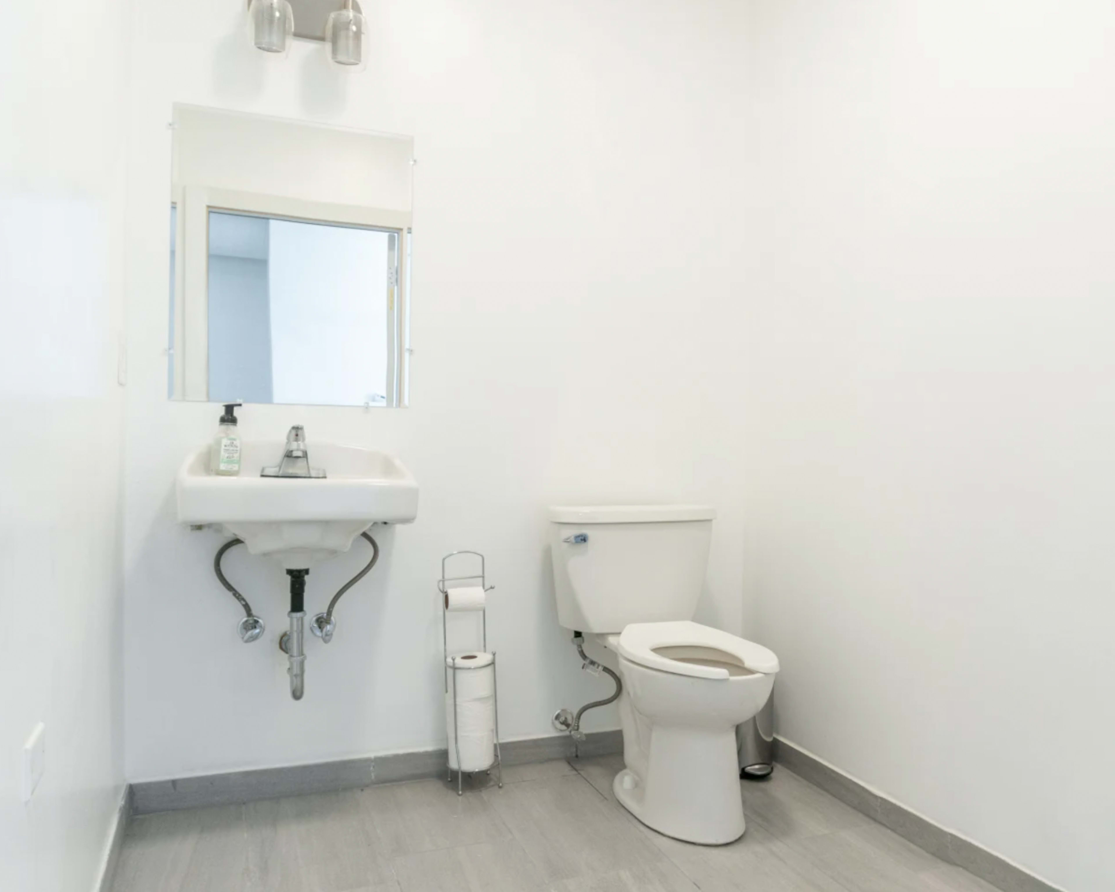 A small bathroom featuring a toilet, a sink with a mirror above it, and a roll of toilet paper on a holder.