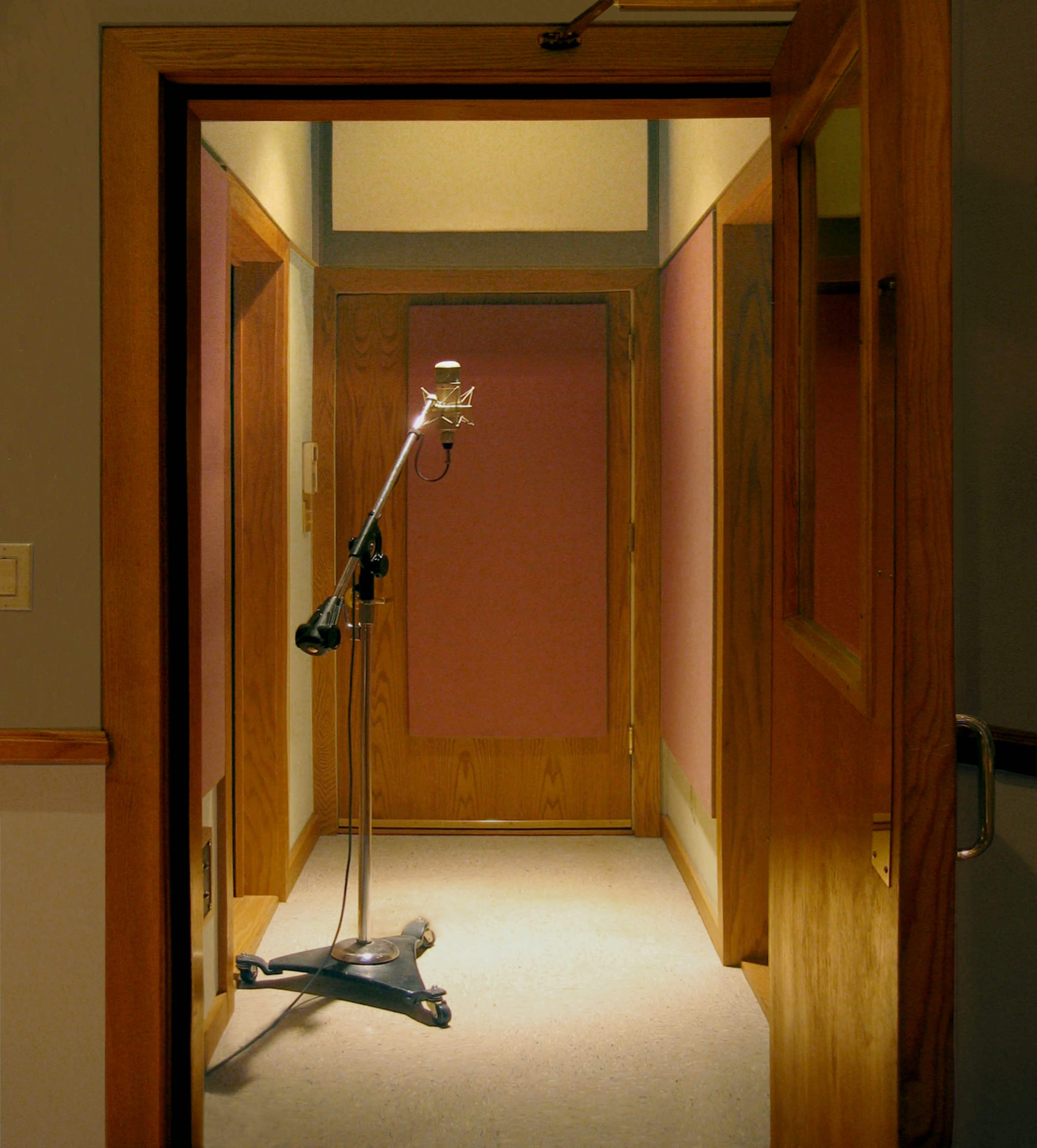 A microphone on a stand is positioned in a hallway leading to two closed doors with wooden frames.