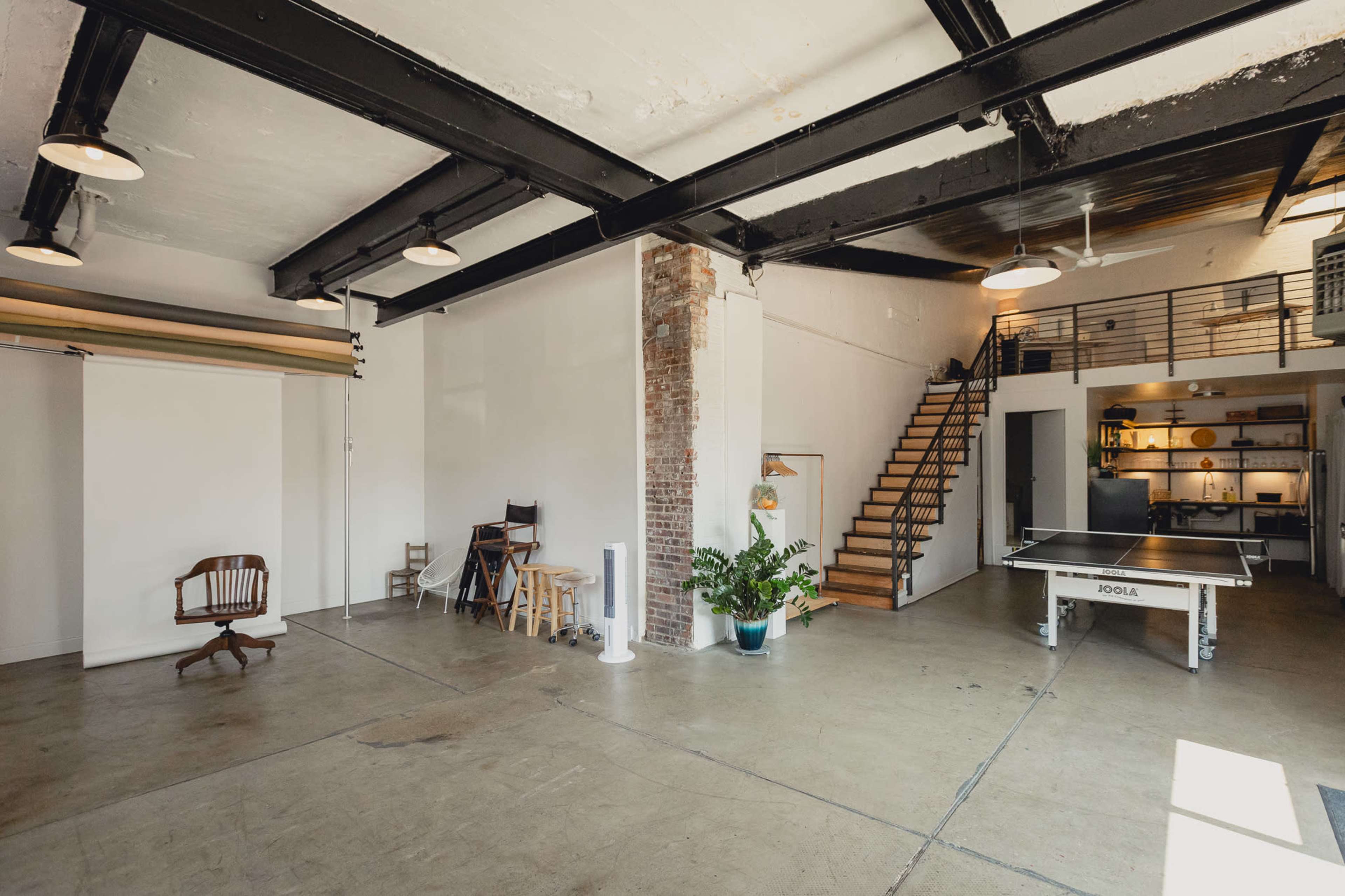 A spacious, industrial-style interior with exposed beams, a staircase, and a ping-pong table.