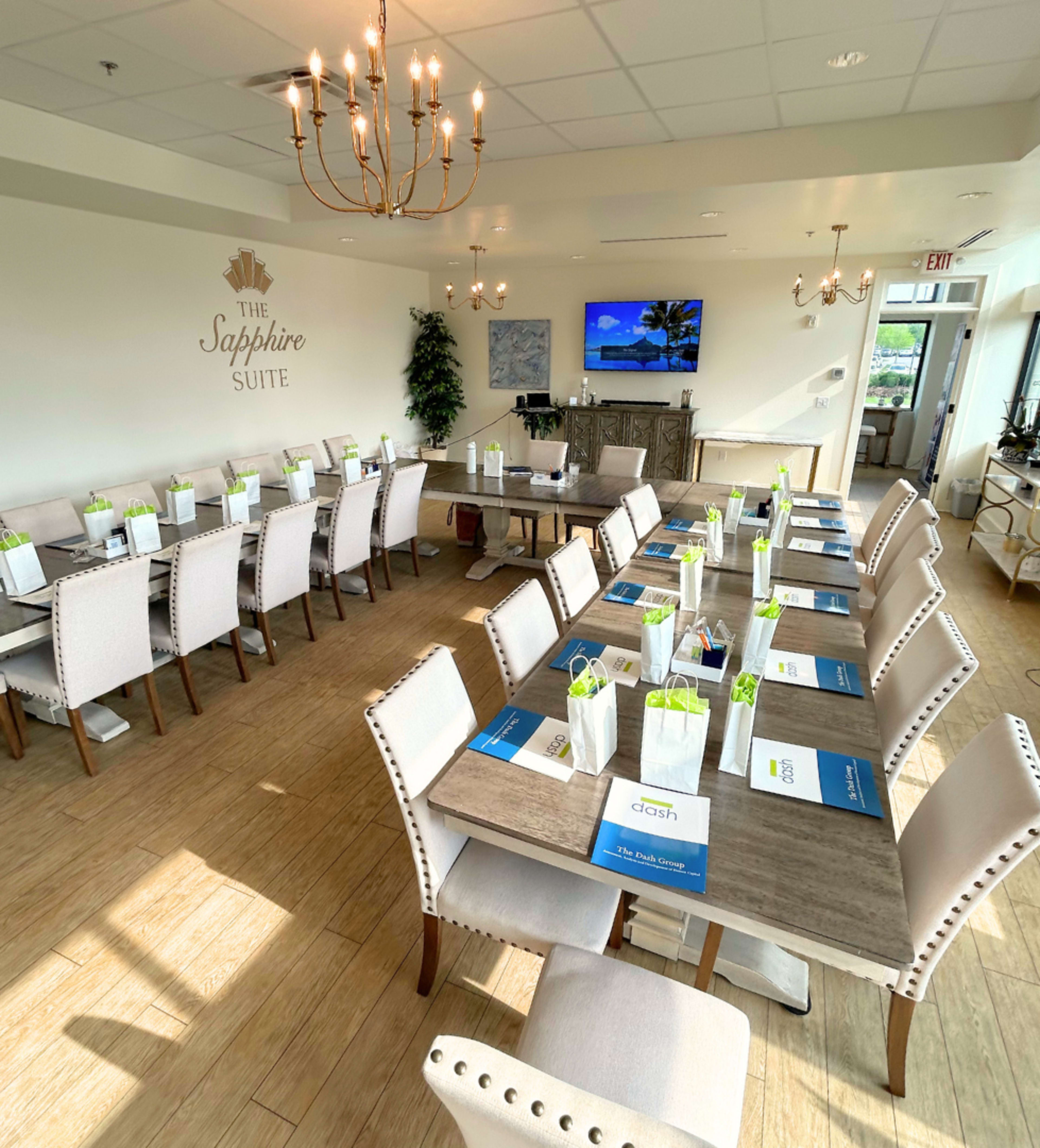 The image shows a well-arranged conference room with several tables set up for a meeting, featuring chairs, placemats, and small gift bags on each table.