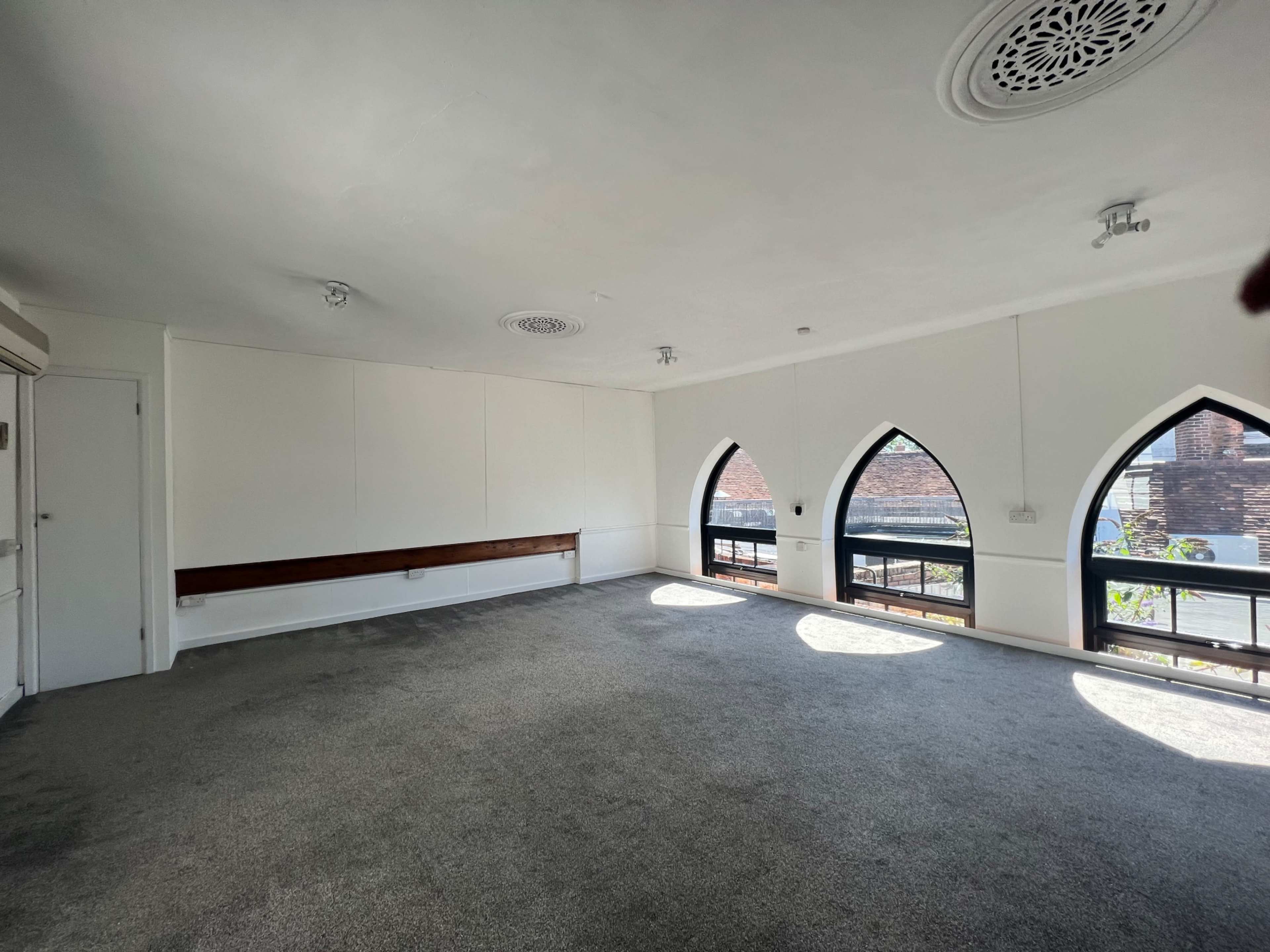 A spacious room with carpeted floors and large arched windows allowing light to enter.