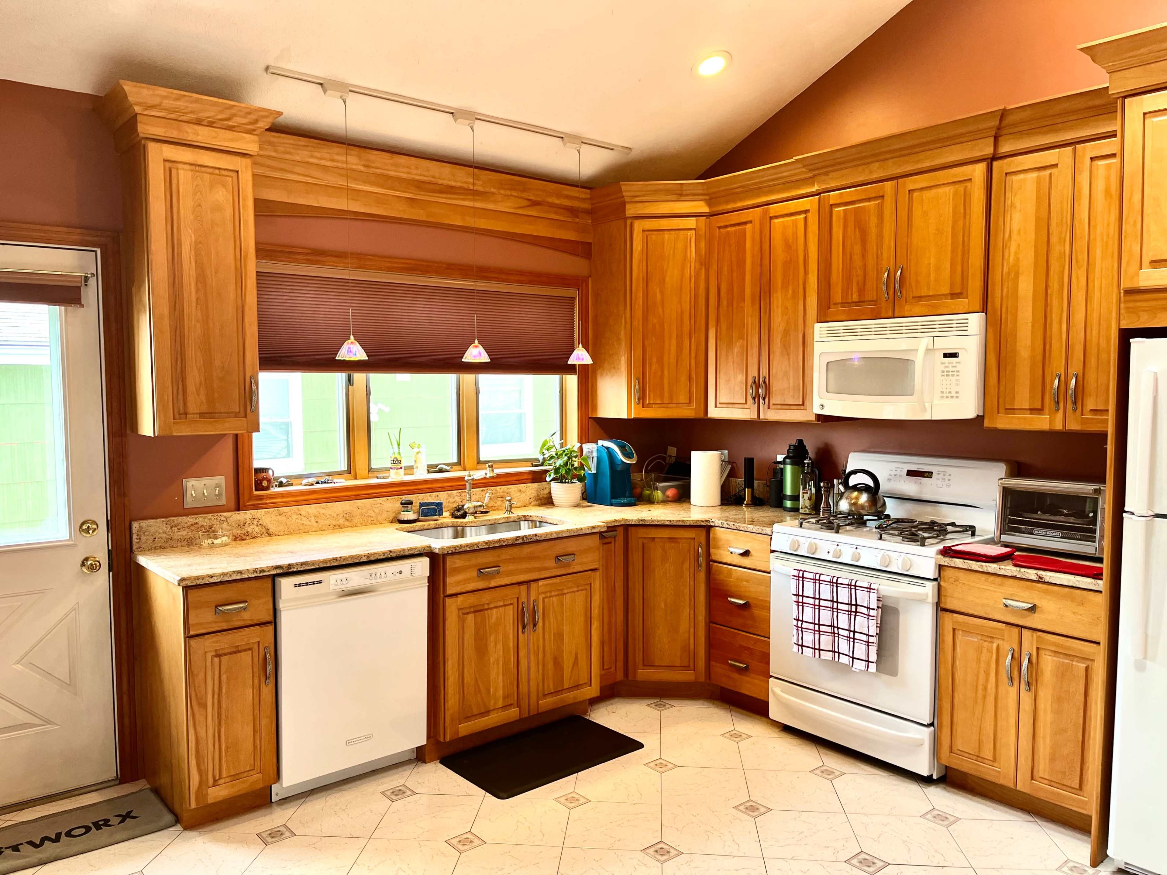 The image shows a well-organized kitchen with wooden cabinets, a white stove, and a countertop featuring a small plant and kitchen appliances.