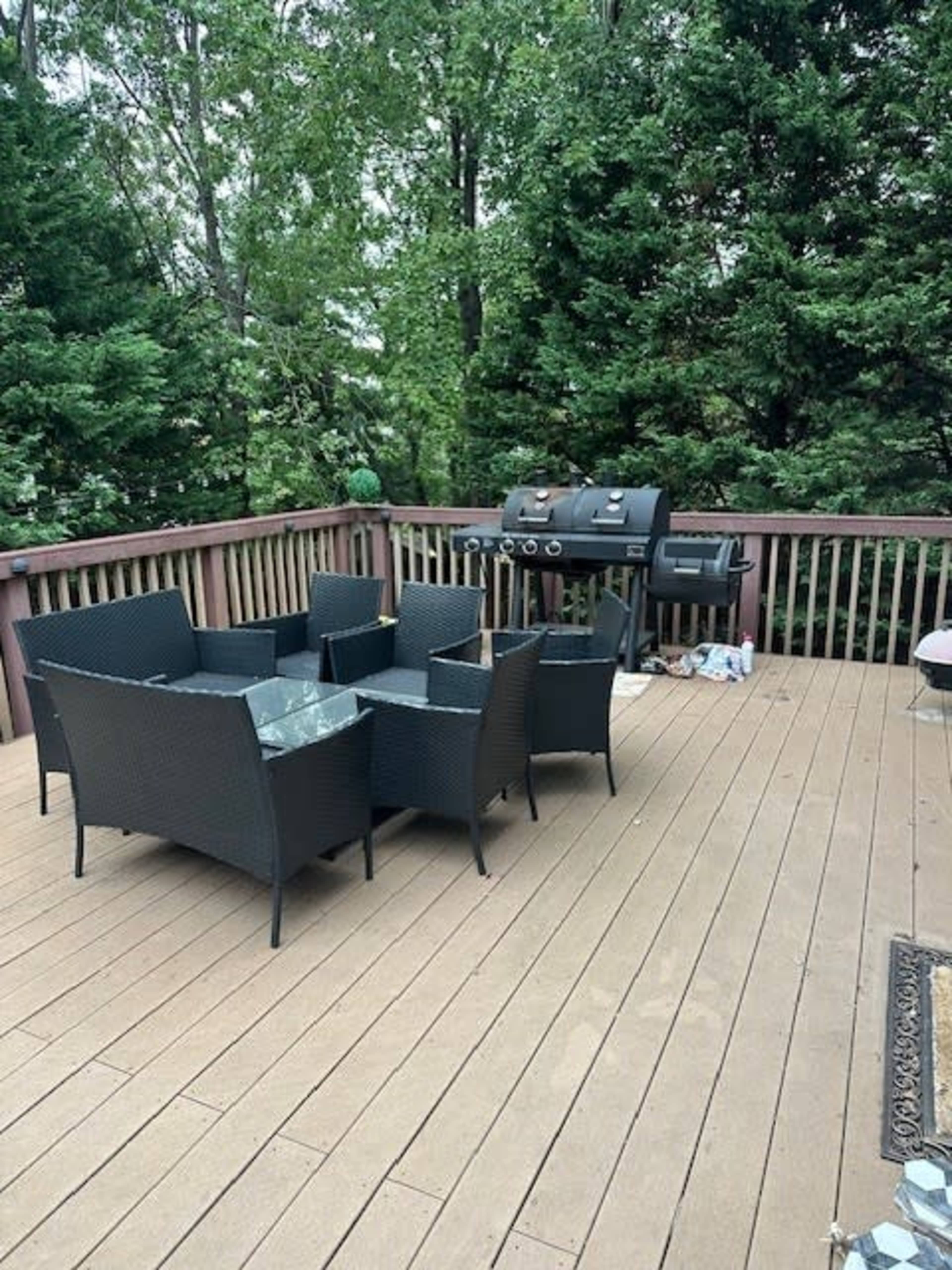 A deck features a set of black wicker furniture and a barbecue grill, surrounded by trees.