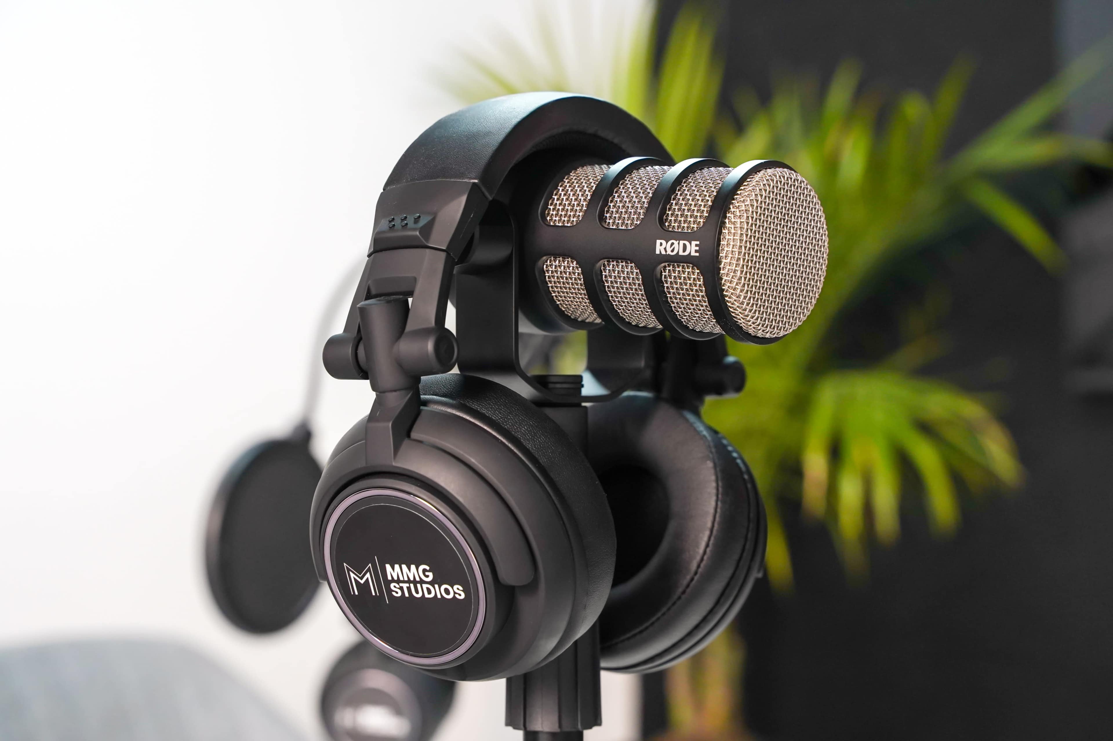 A pair of black headphones and a Rode microphone are displayed on a stand in a studio setting.
