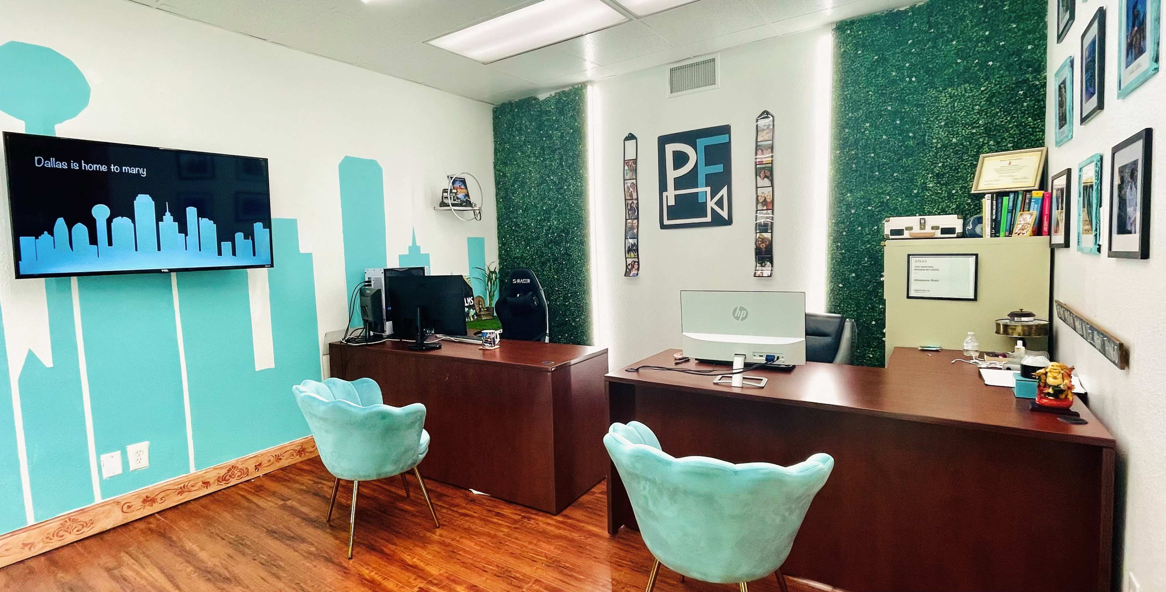 An office space features a desk with a computer and a television displaying a presentation, surrounded by green accent walls and a decor of framed pictures.