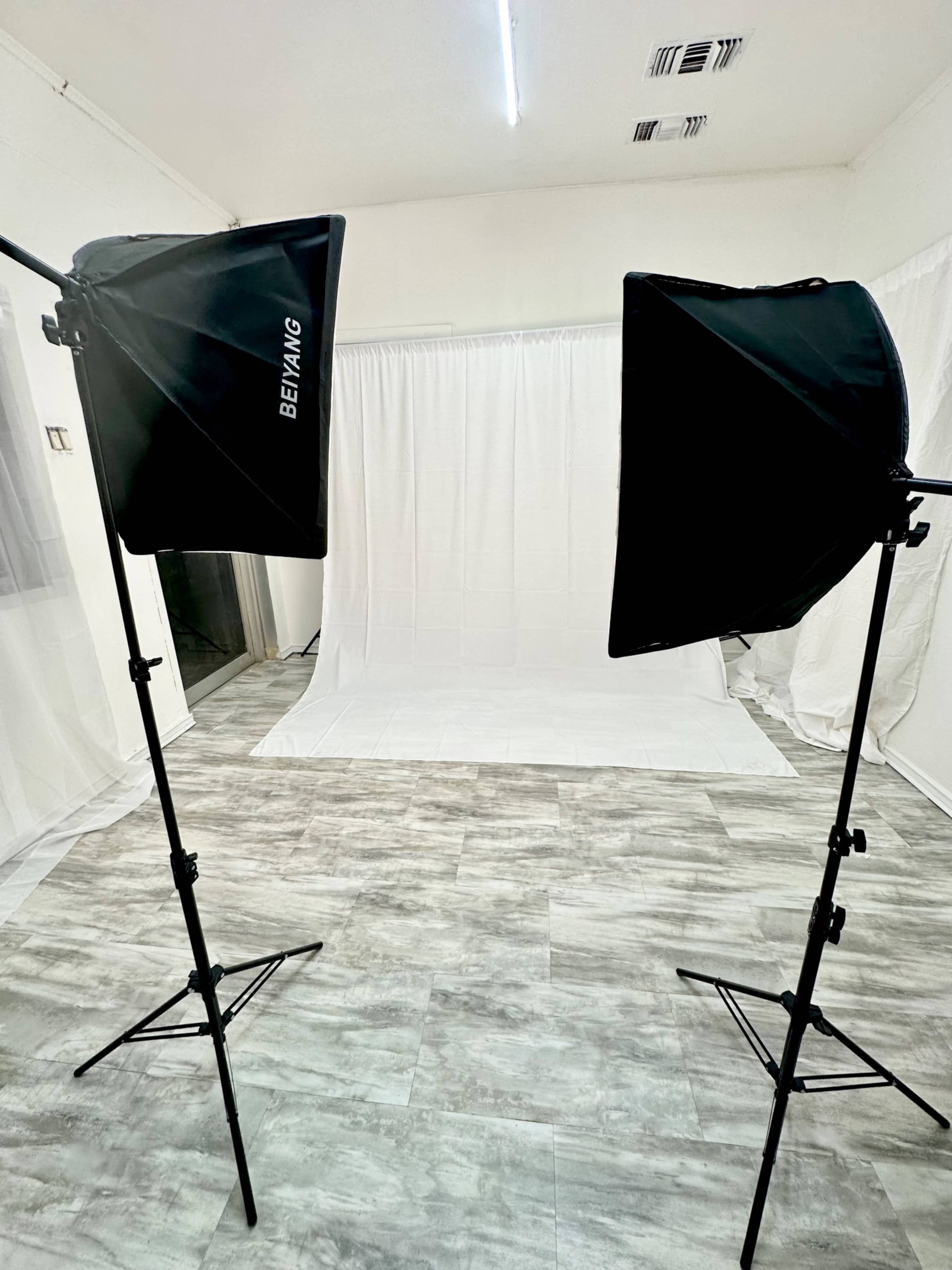 A photography studio with two light stands and a white backdrop set against a floor with gray tiling.