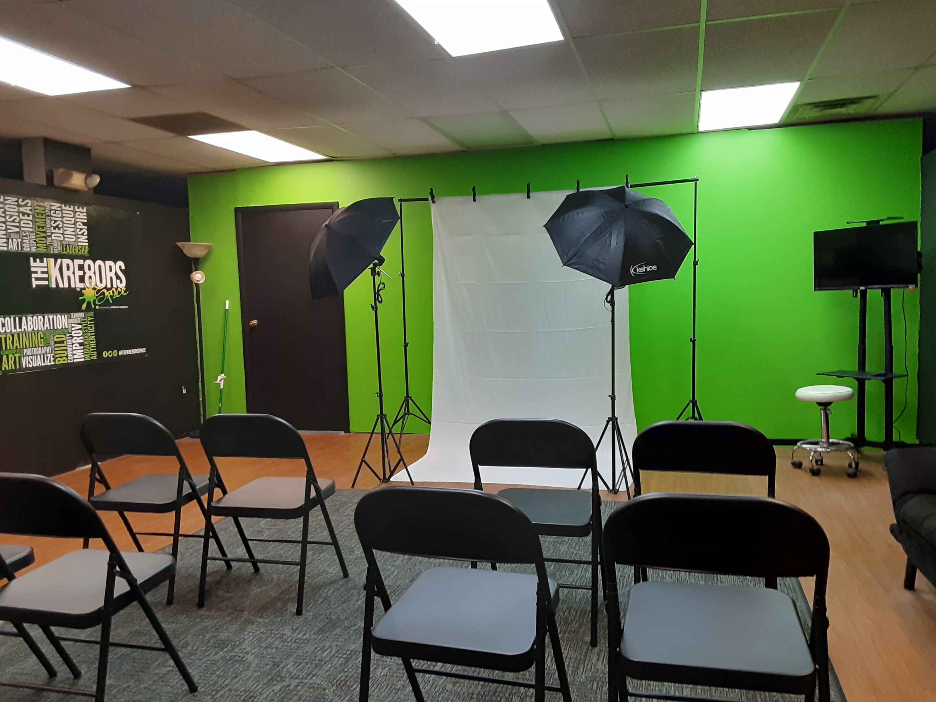 A photography setup featuring a white backdrop and two black umbrella lights, with rows of empty black chairs arranged in front of it.
