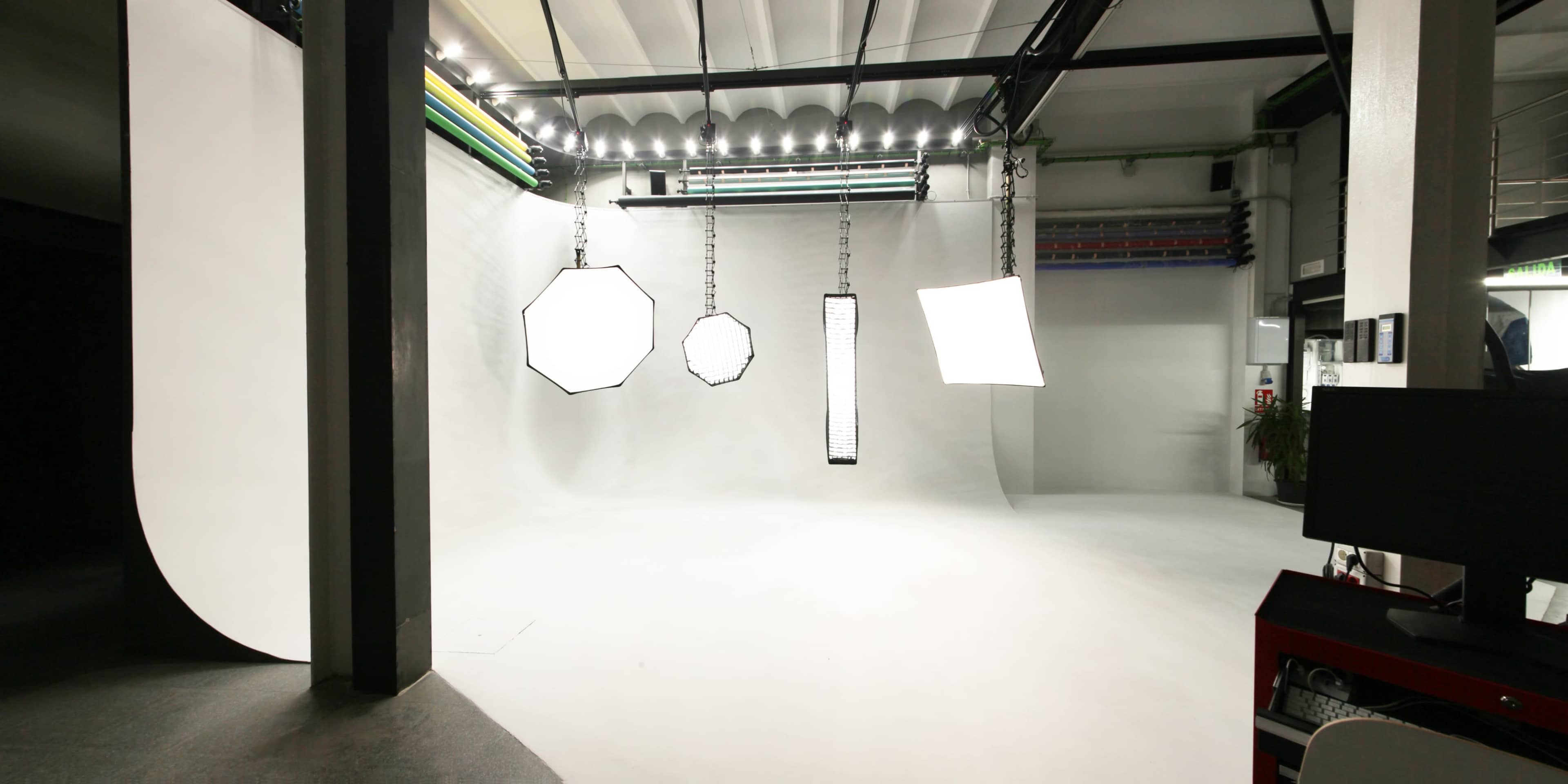 A photography studio features a seamless white backdrop with various hanging light sources.