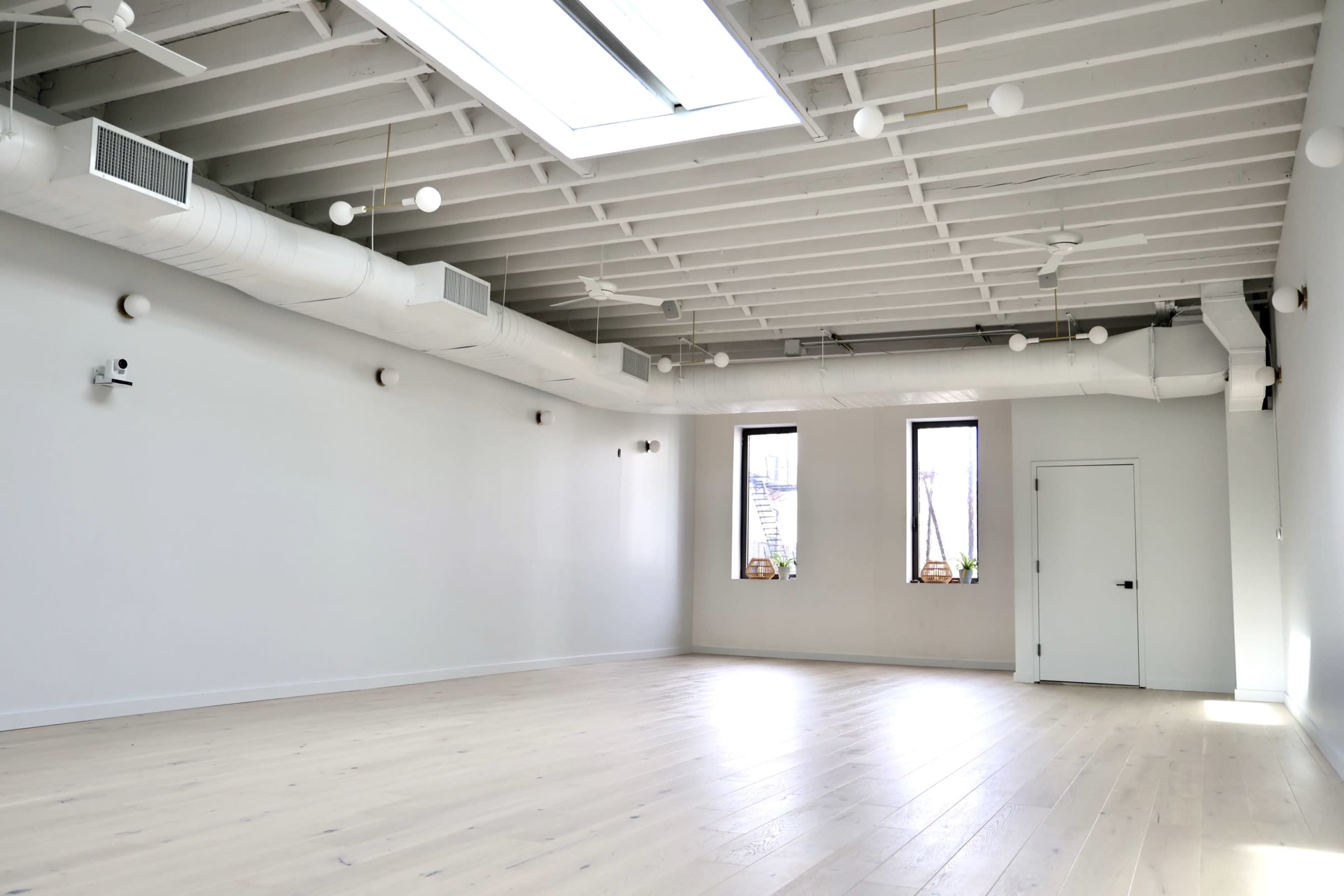 A spacious, uncluttered room with white walls, wooden floors, and large windows.