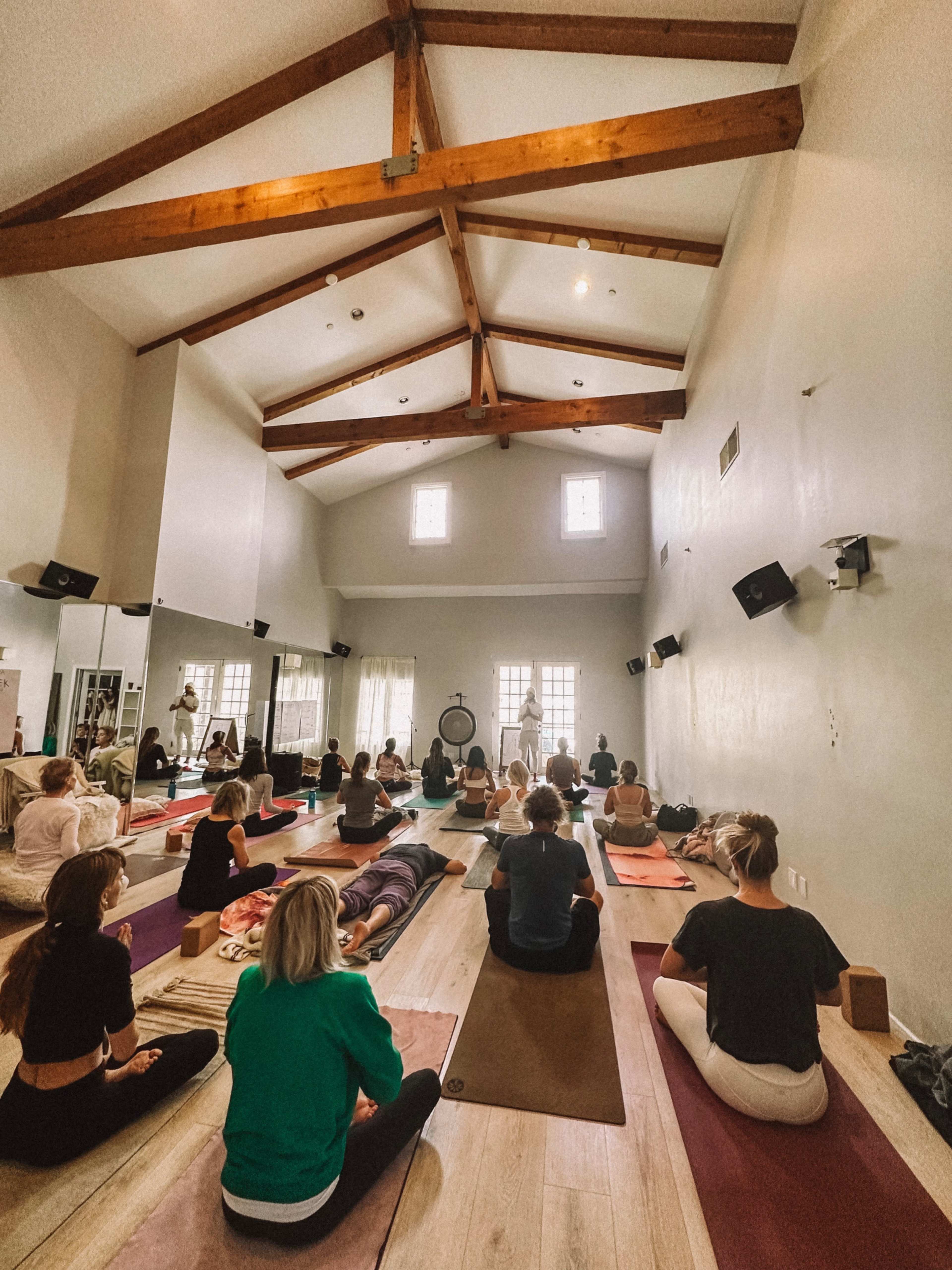 A group of people is practicing yoga in a spacious studio with high ceilings and wooden beams.